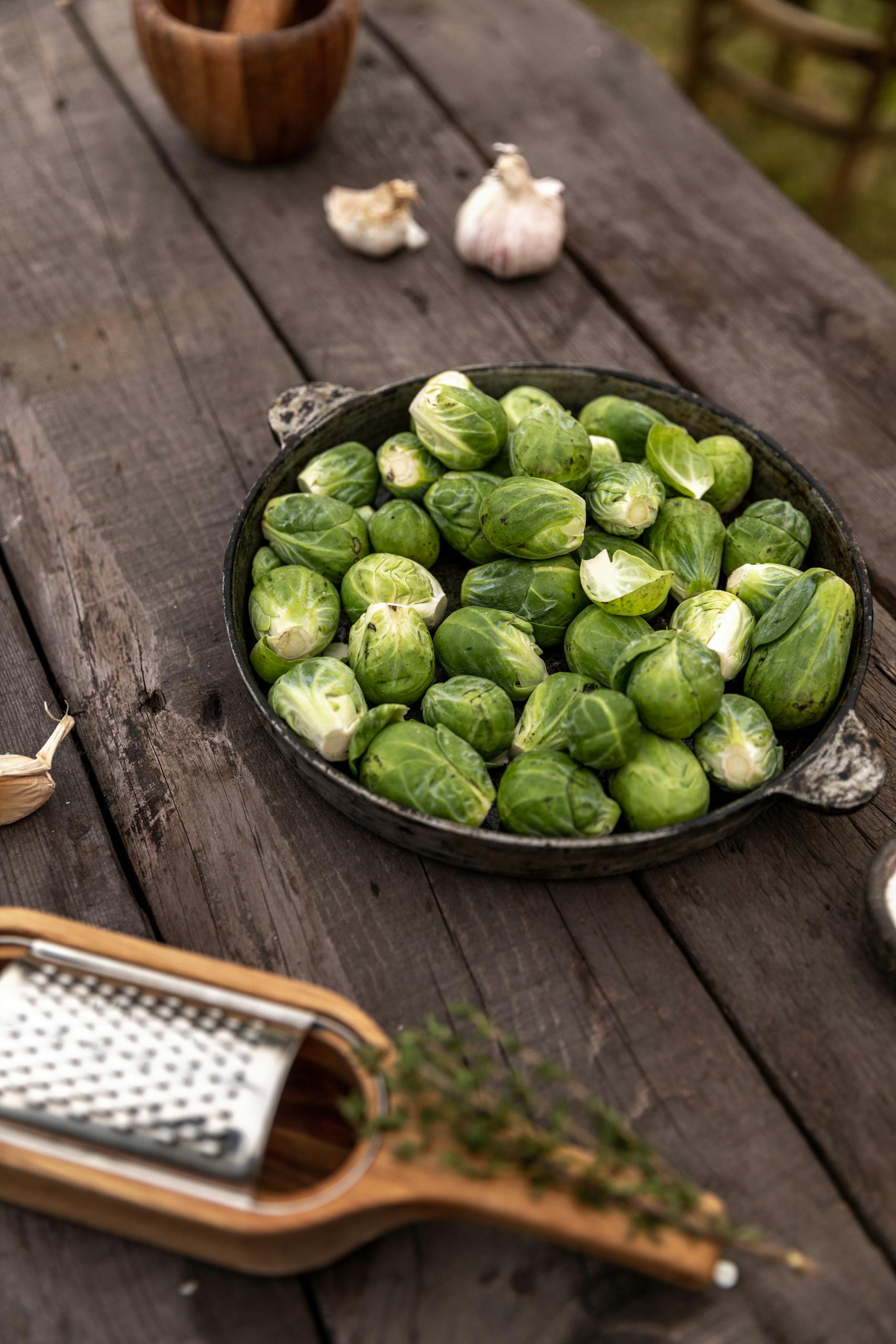 A rustic setting with Brussels sprouts, garlic, and a grater on a wooden surface.