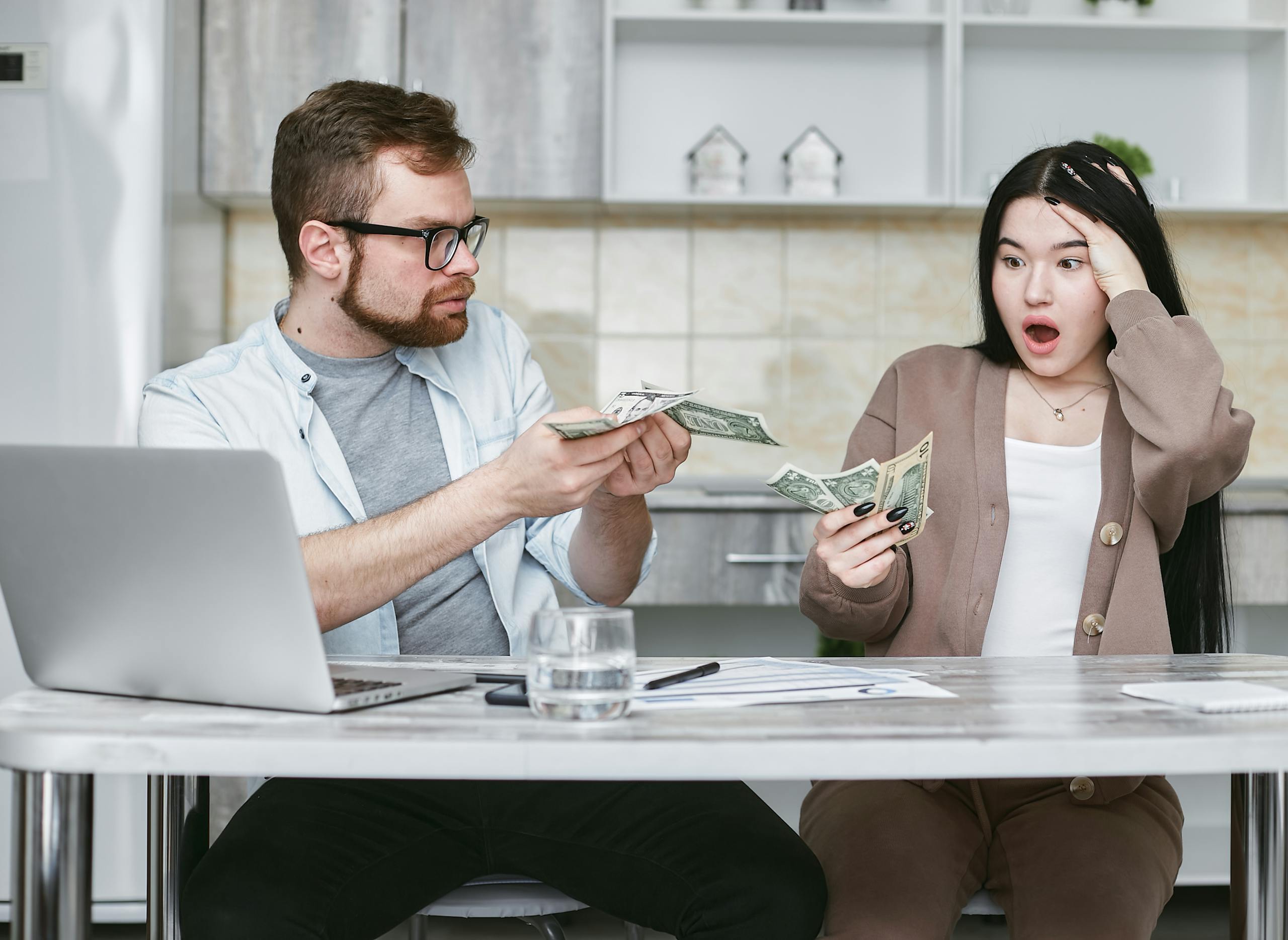 A shocked couple sitting at a table counting cash, illustrating financial surprise.