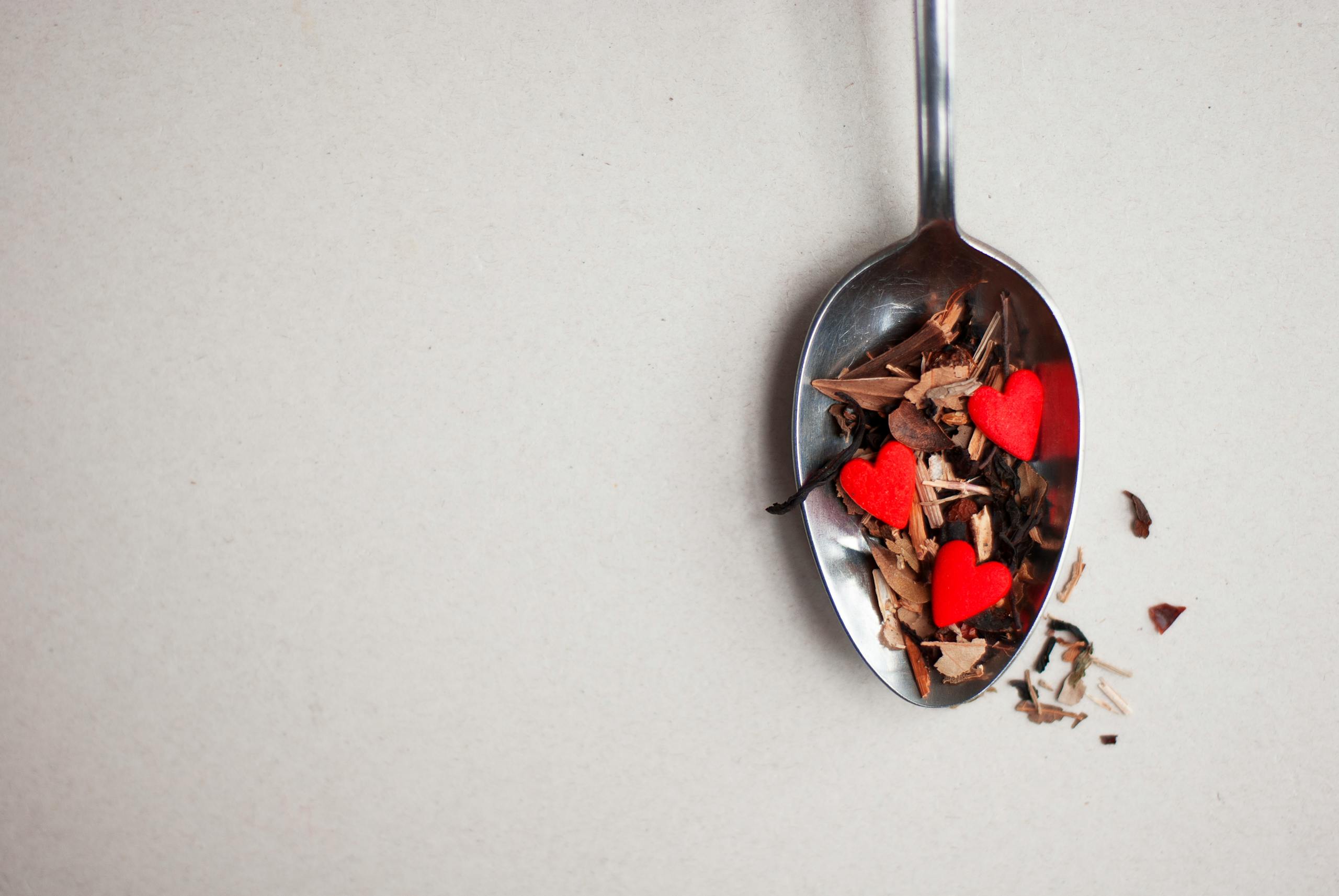 A spoon filled with tea leaves and red heart decorations. Perfect for Valentine's themes.