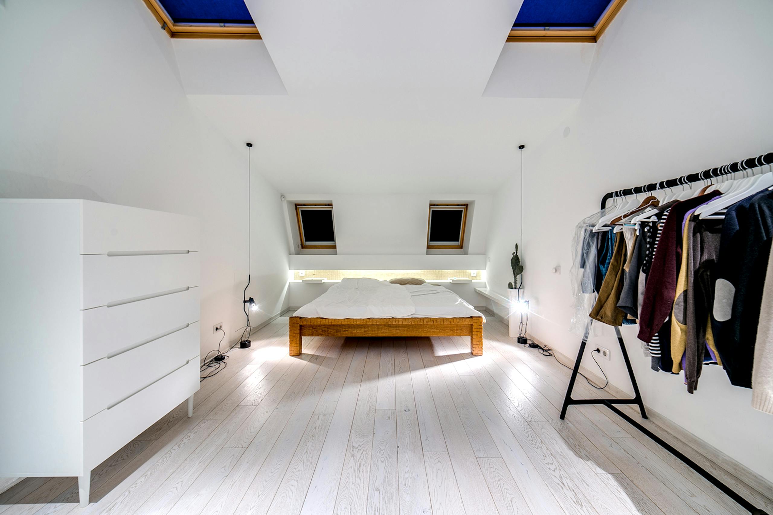 A stylish white minimalist bedroom featuring skylights, wooden bed frame, and chic decor.