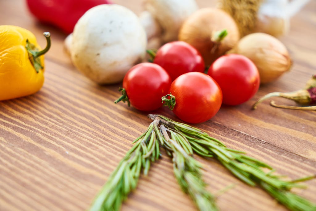 A variety of fresh vegetables including tomatoes, bell pepper, and rosemary on a wooden table.
