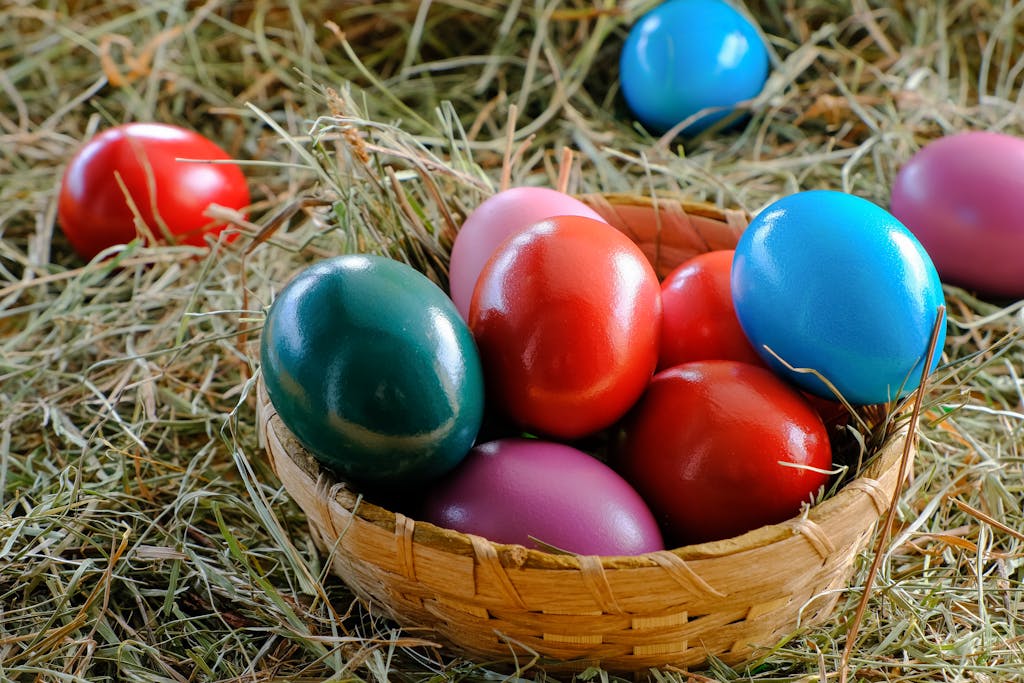 A vibrant display of colorful Easter eggs in a woven basket, set on a bed of hay.