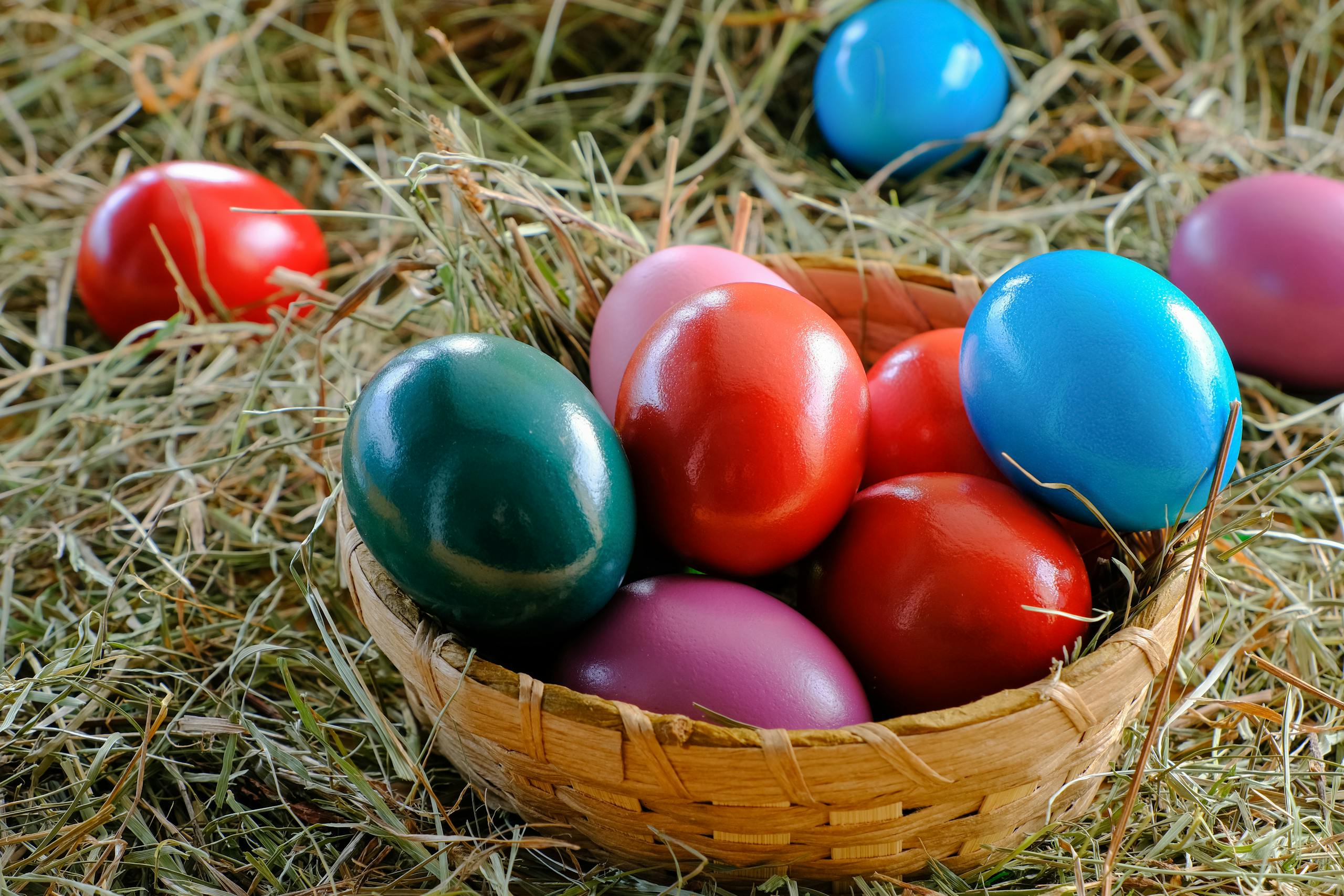 A vibrant display of colorful Easter eggs in a woven basket, set on a bed of hay.