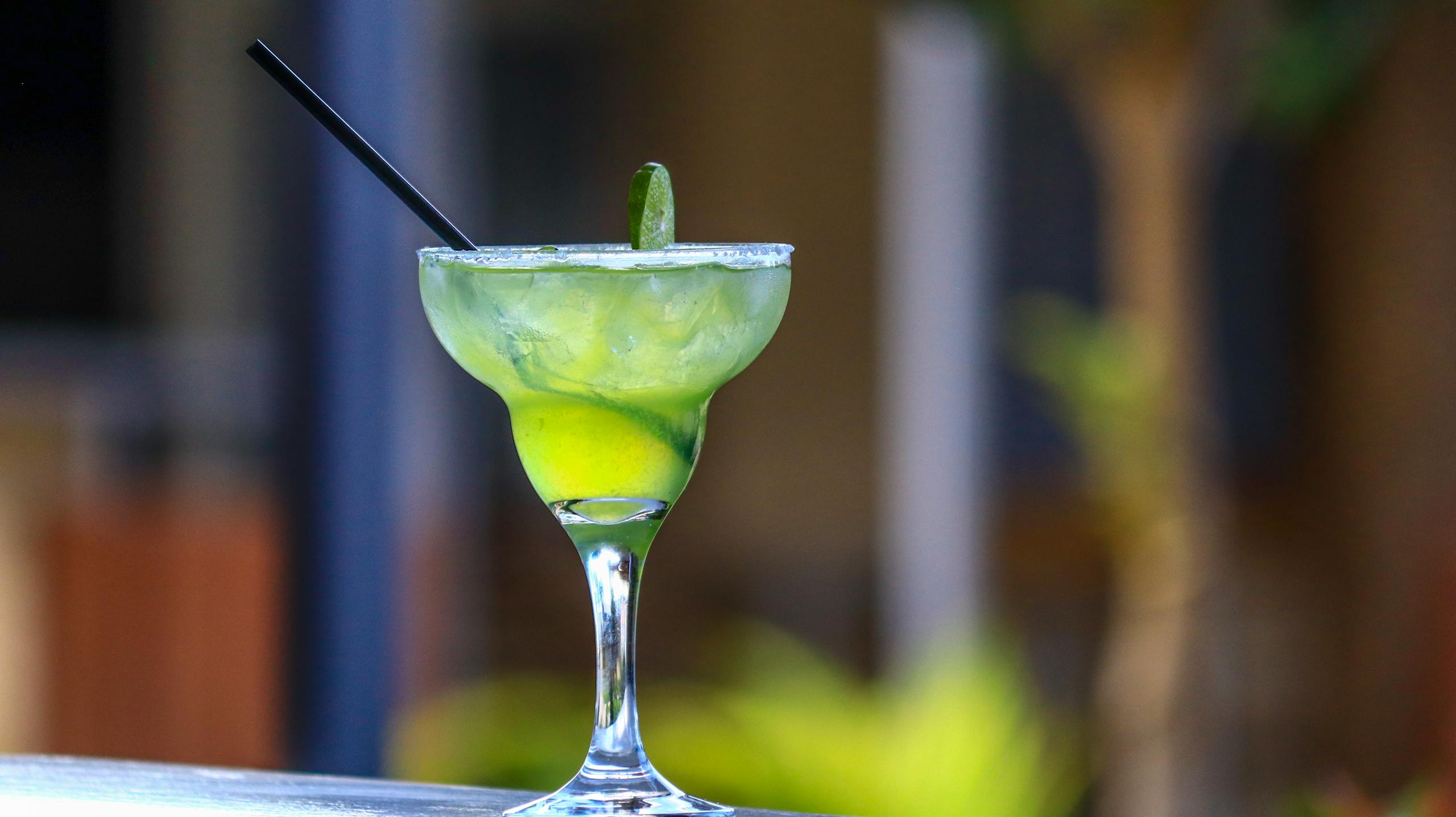 A vibrant lime margarita with a black straw, perfect for summer refreshment.