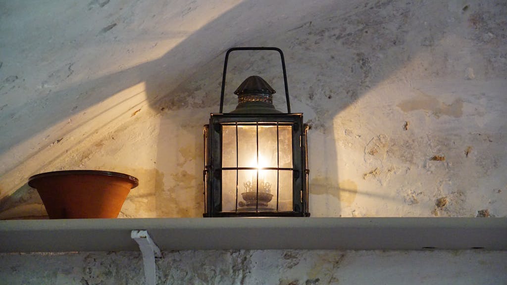 A vintage lantern casting warm light and shadows in a rustic interior setting.
