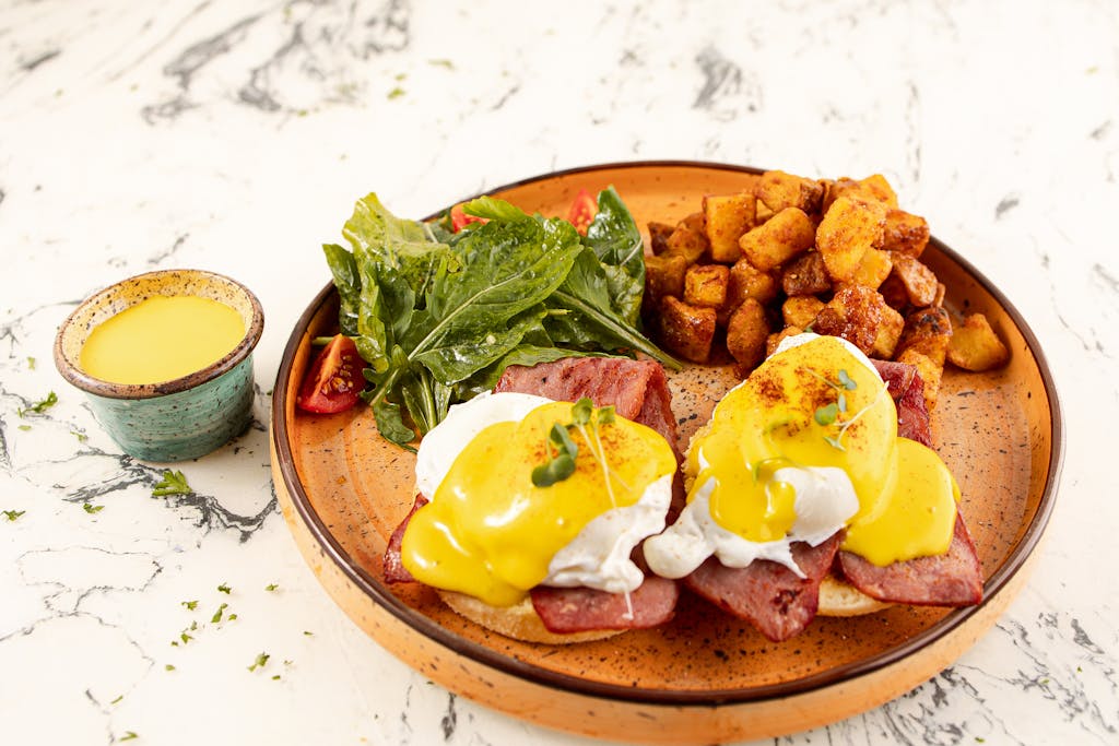 A visually appealing Eggs Benedict with salad and seasoned potatoes, perfect for breakfast lovers.