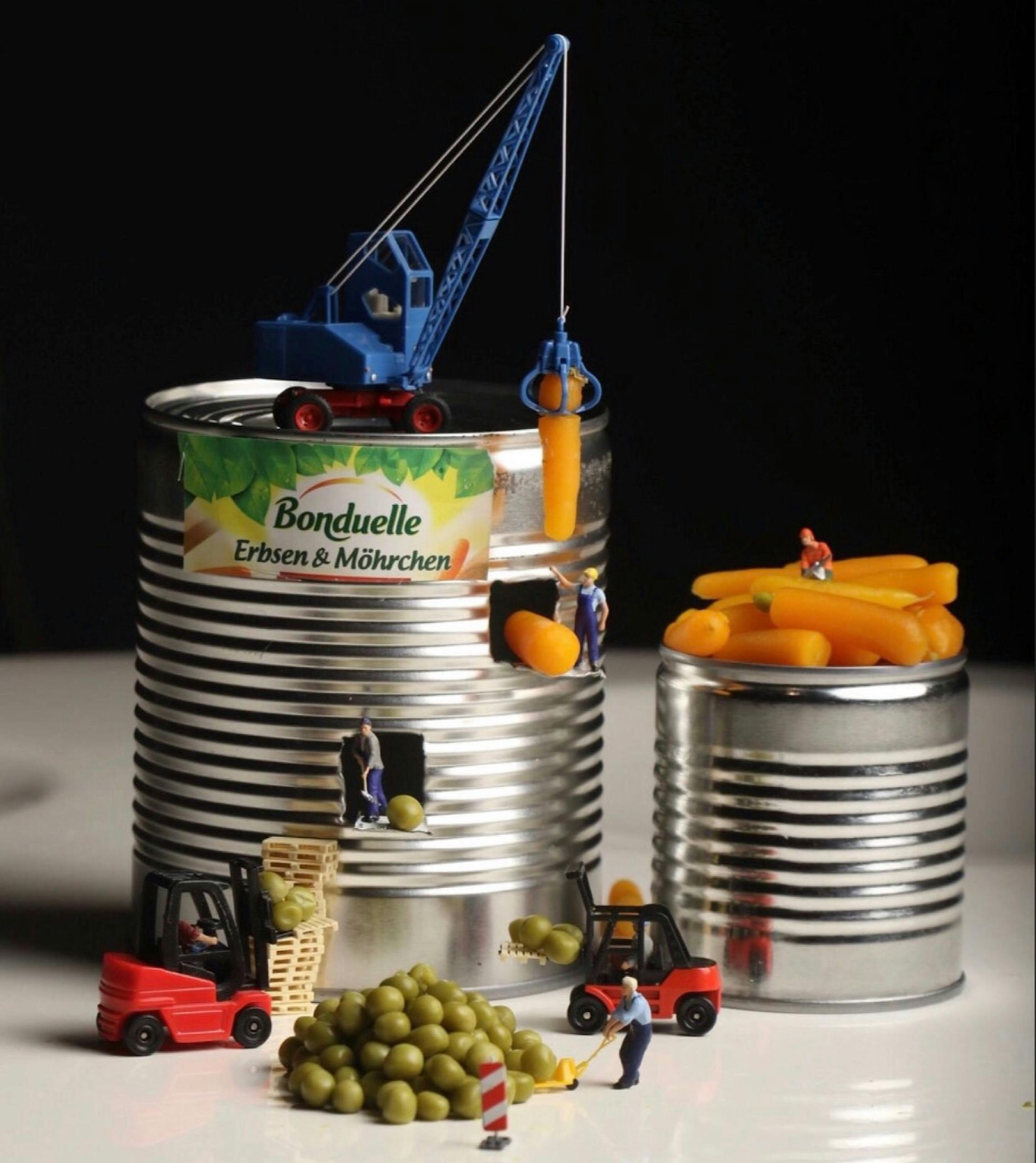 A whimsical scene with toy figures stacking miniature carrots and peas in cans.