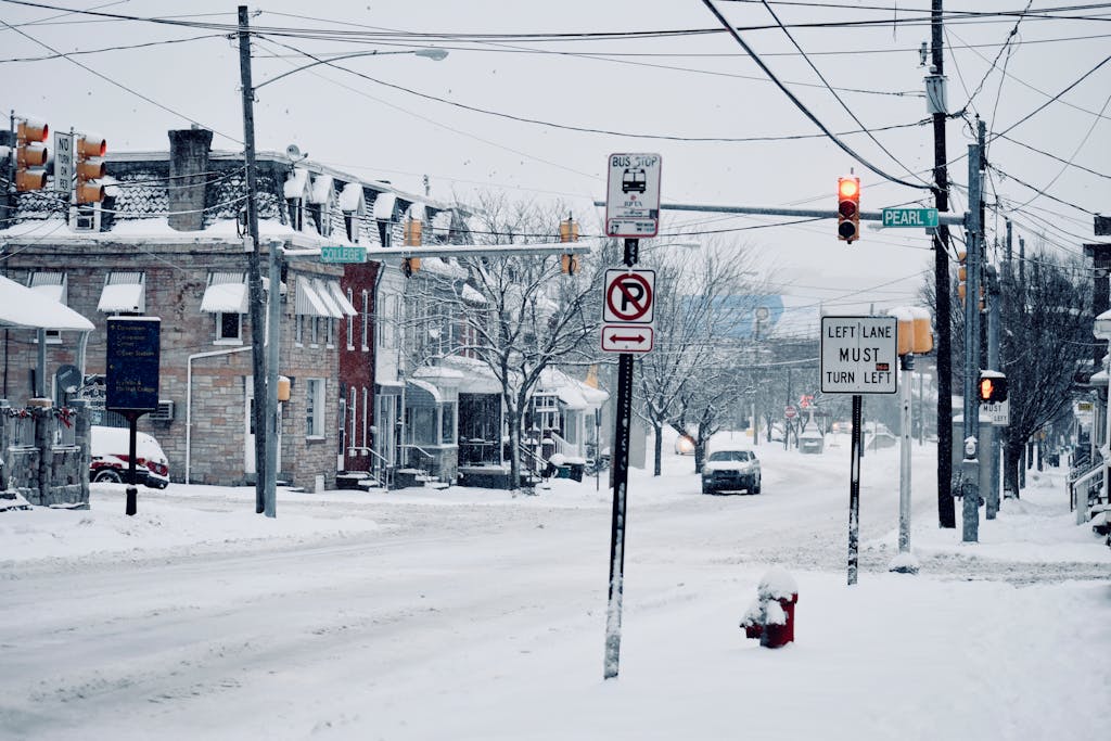 A winter street view in Lancaster, PA showcasing snowy roads, traffic signs, and parked vehicles.