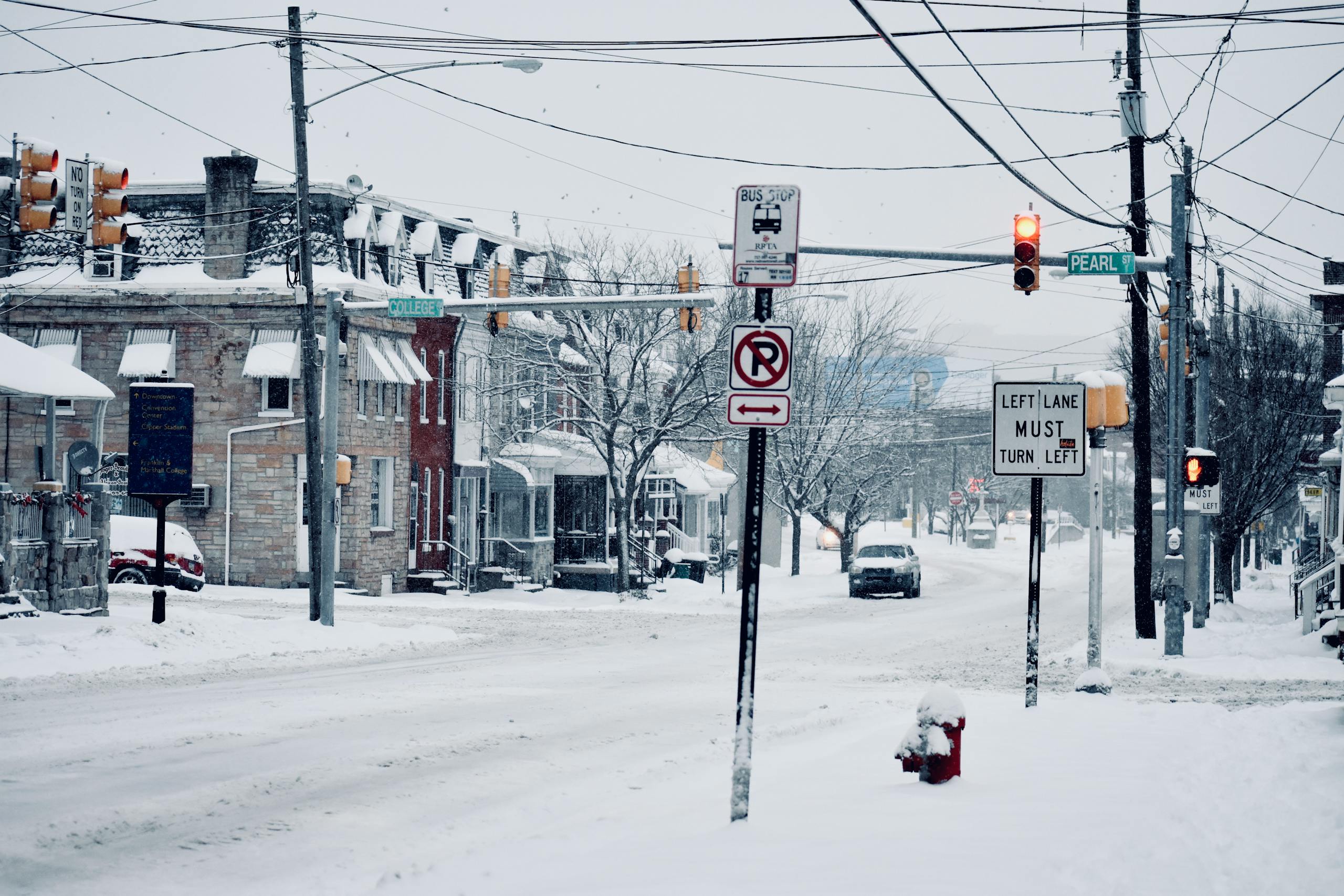 A winter street view in Lancaster, PA showcasing snowy roads, traffic signs, and parked vehicles.