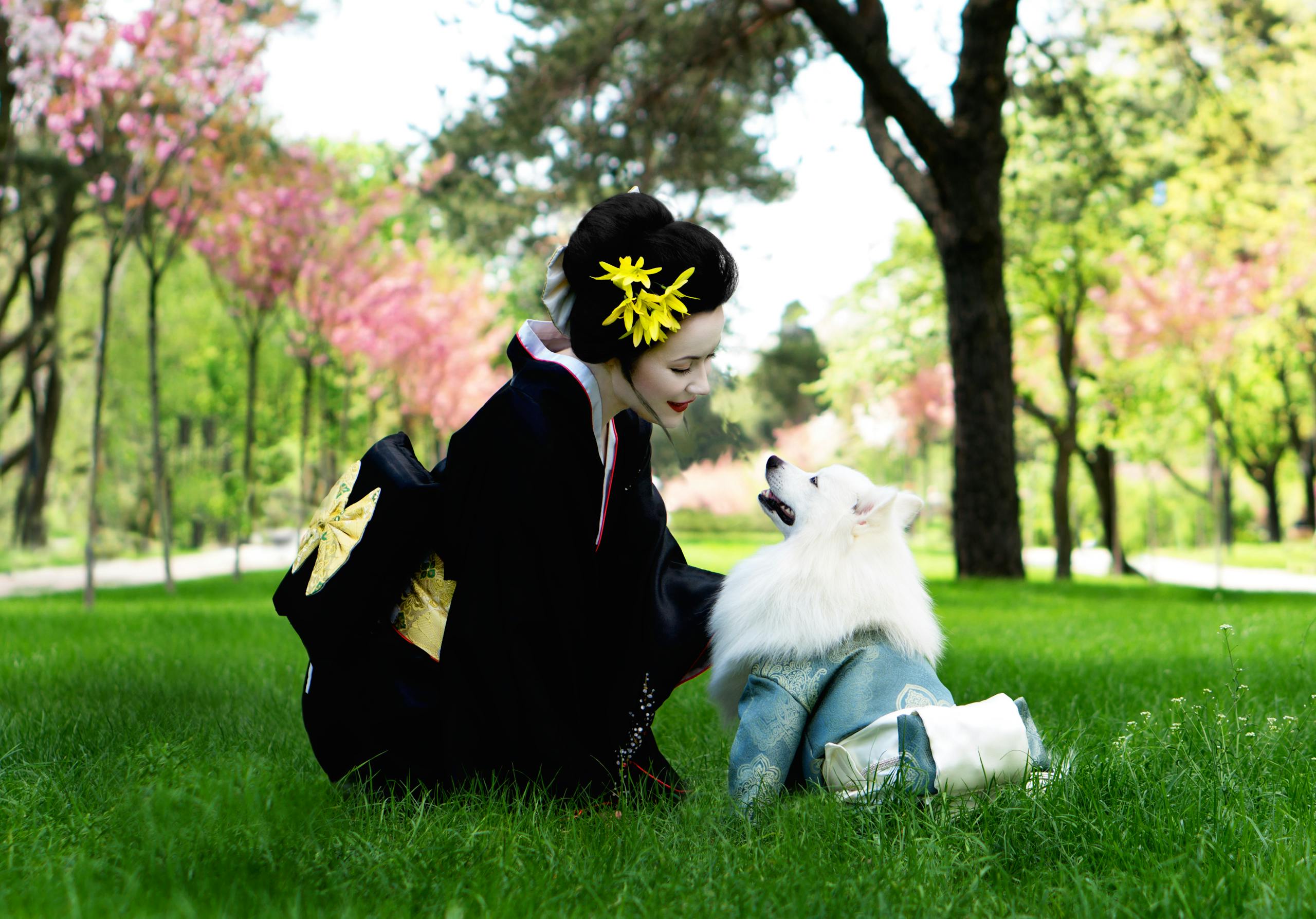 A woman in a kimono shares a moment with a Japanese Spitz in a lush park.
