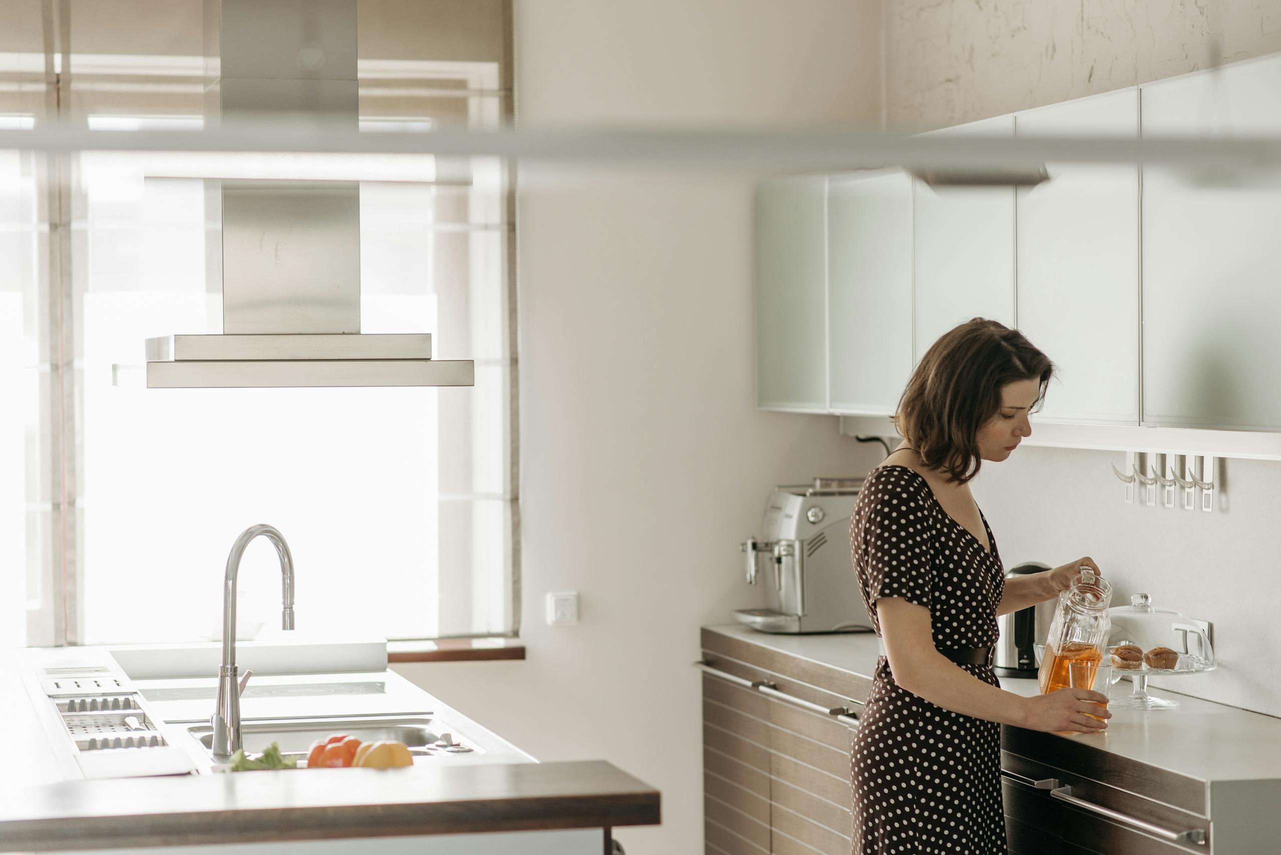 A woman in a polka dot dress pours juice in a contemporary kitchen, showcasing a clean and modern interior design.