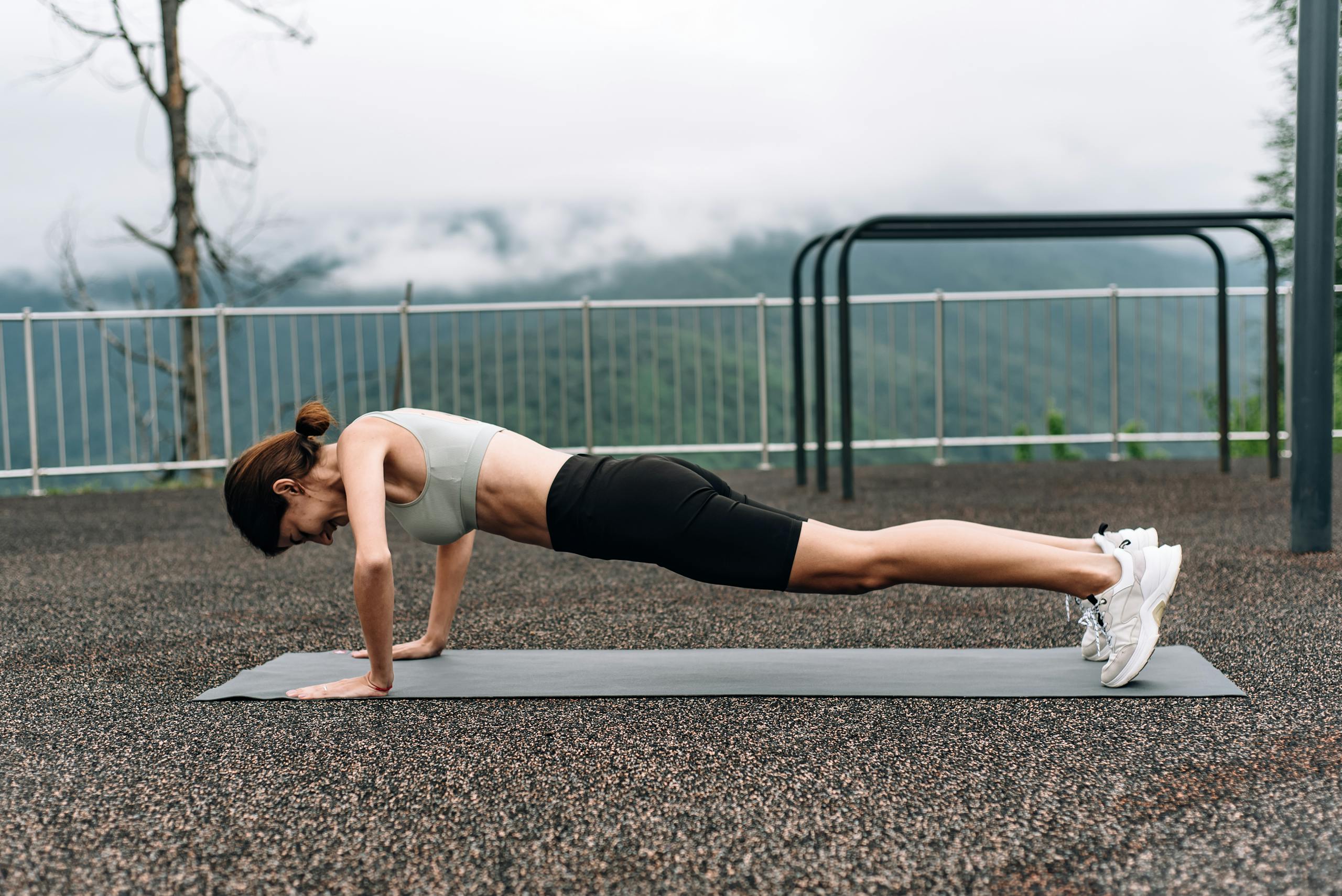 A woman in activewear doing a plank on a yoga mat outdoors, promoting fitness and strength