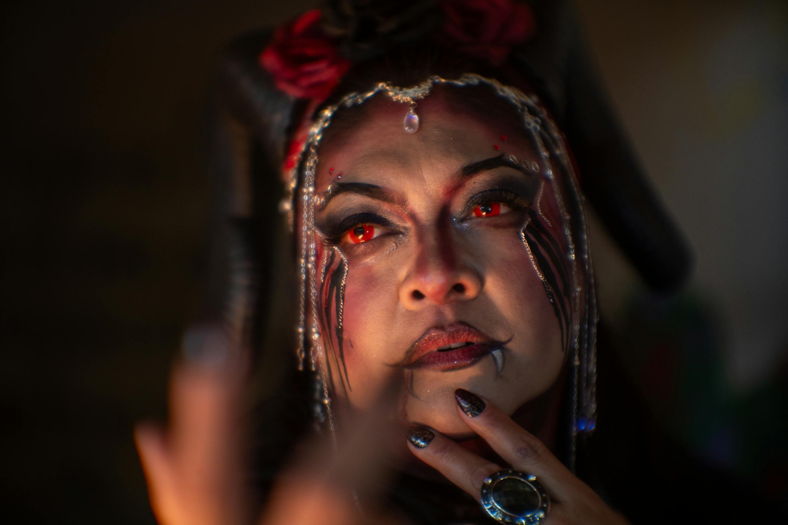 A woman in demon makeup with red eyes and horns, exuding a mystical aura.