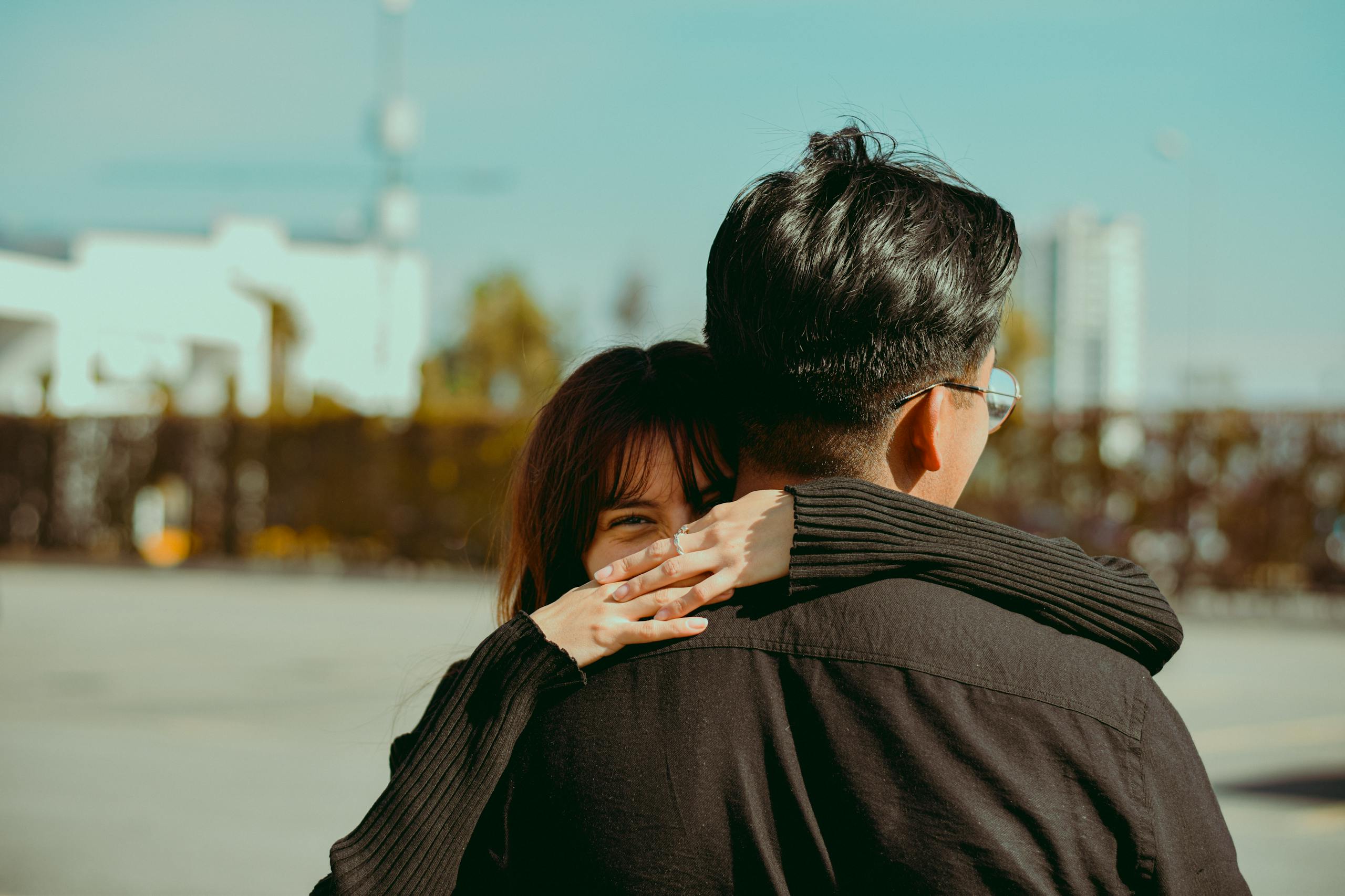 A woman playfully hugging a man outdoors in an urban setting, with a joyful smile.