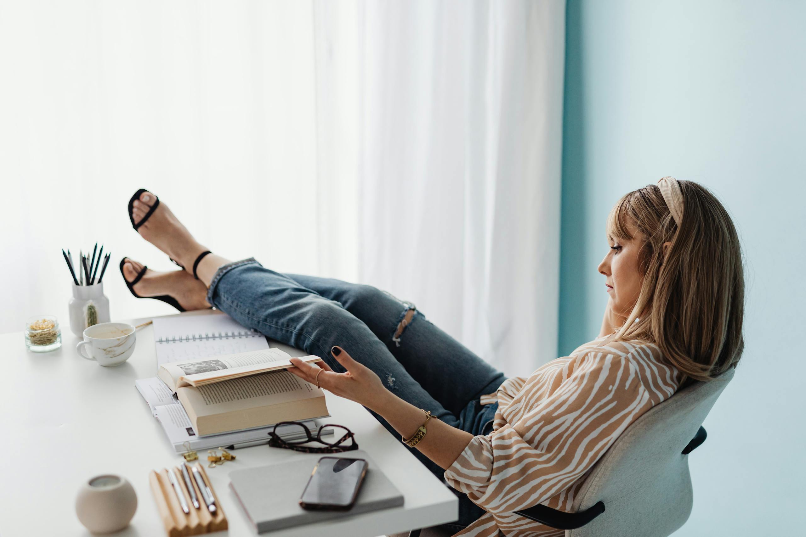 A woman rests with her feet on the desk, reading in a bright, modern office.