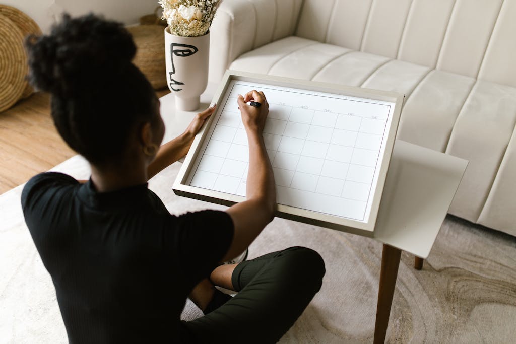 A woman sits on the floor at home, planning her schedule using a calendar on a small table.