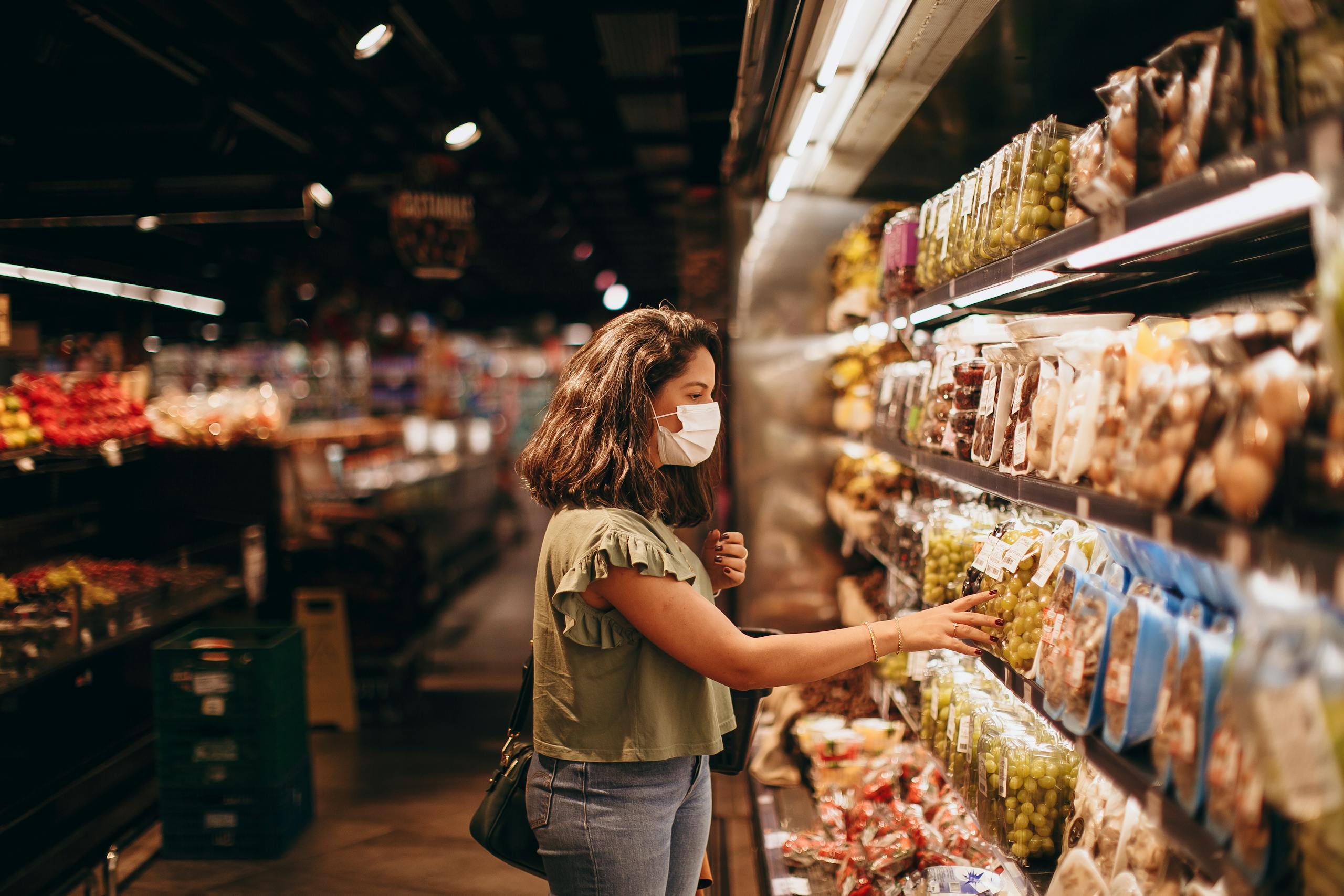 A woman wearing a mask shops for groceries in a supermarket aisle.