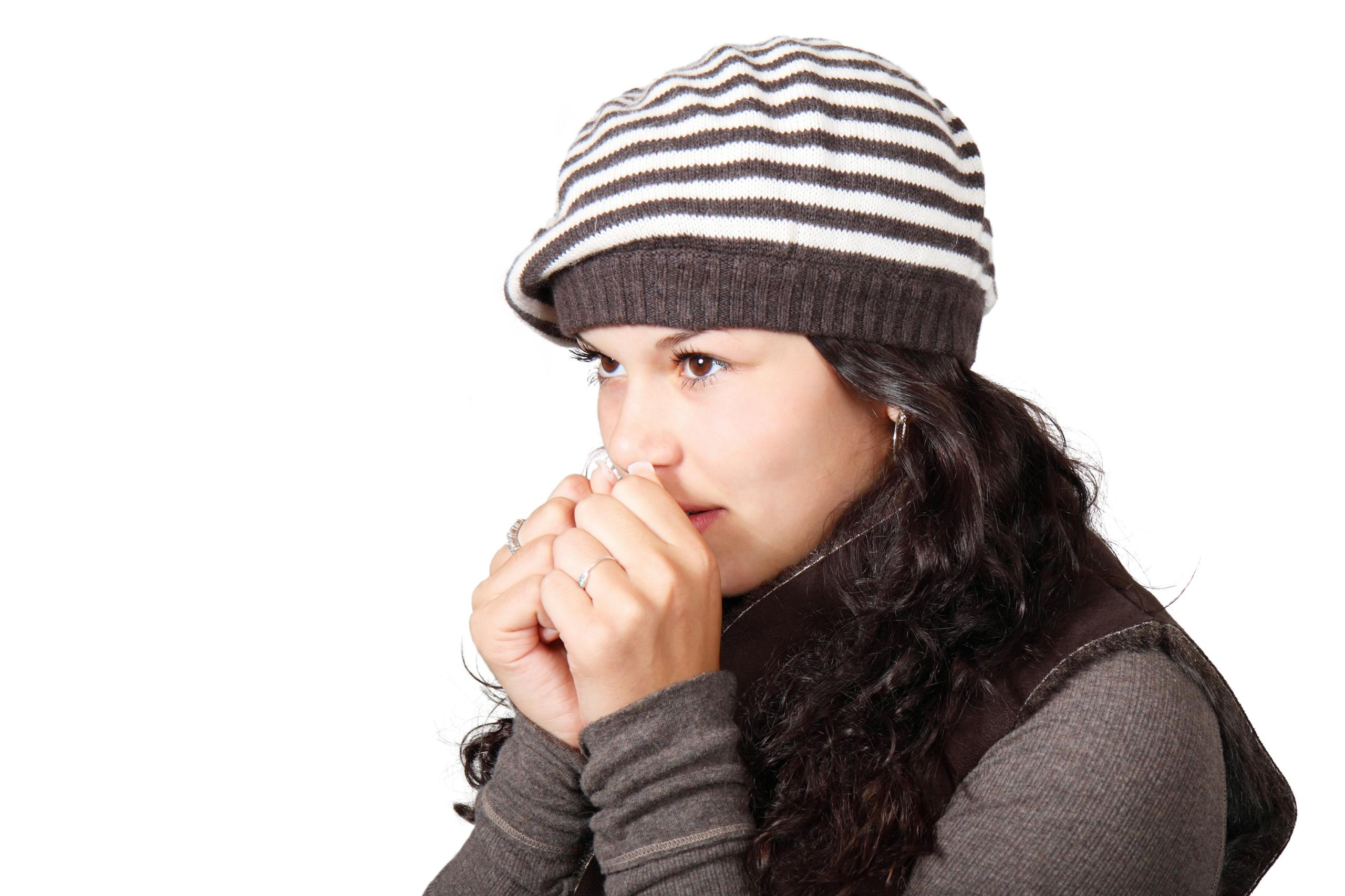 A woman wearing a striped beanie and winter clothing, looking chilly on a cold day.