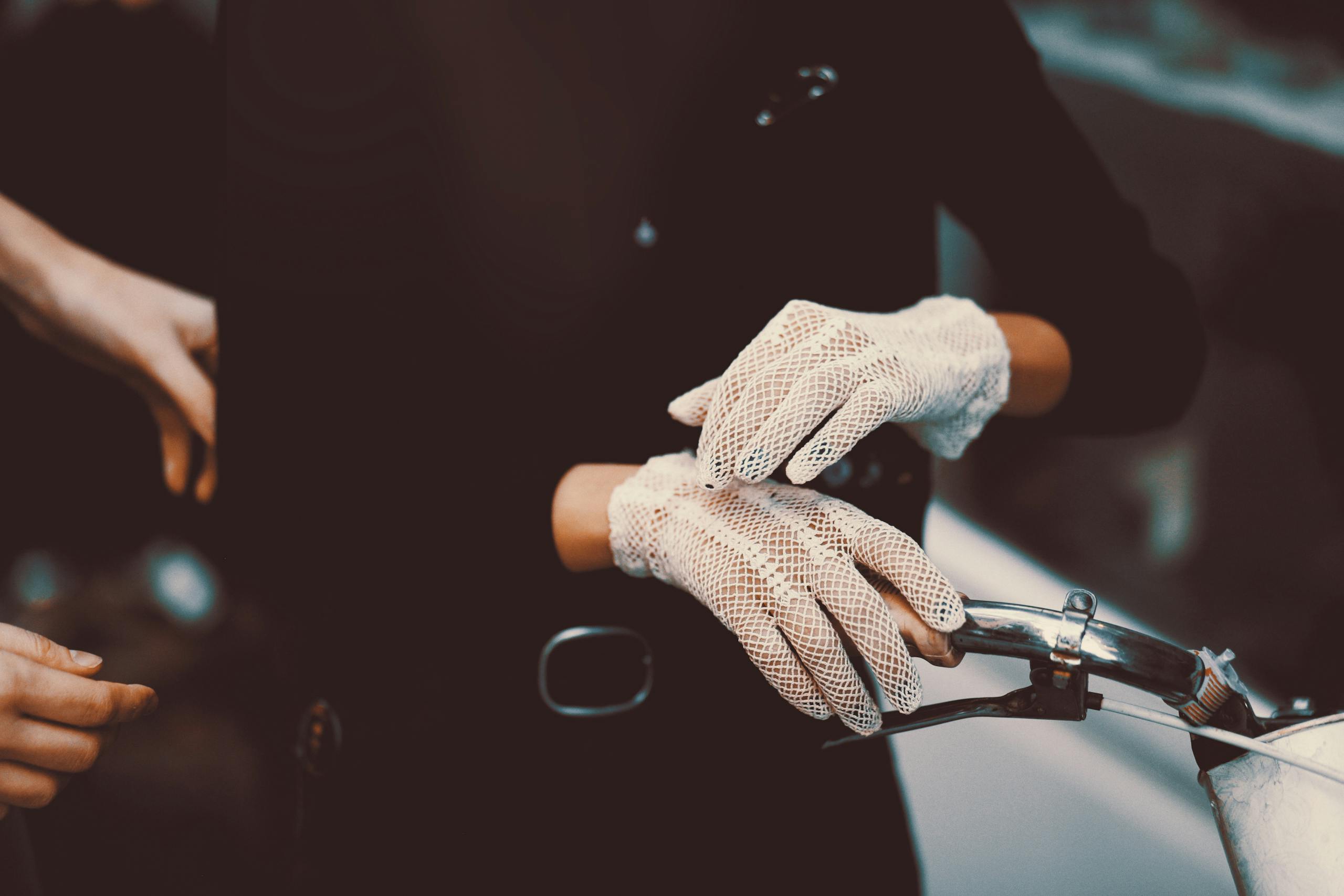 A woman wearing lace gloves holds a vintage bicycle handlebar, exuding elegance.