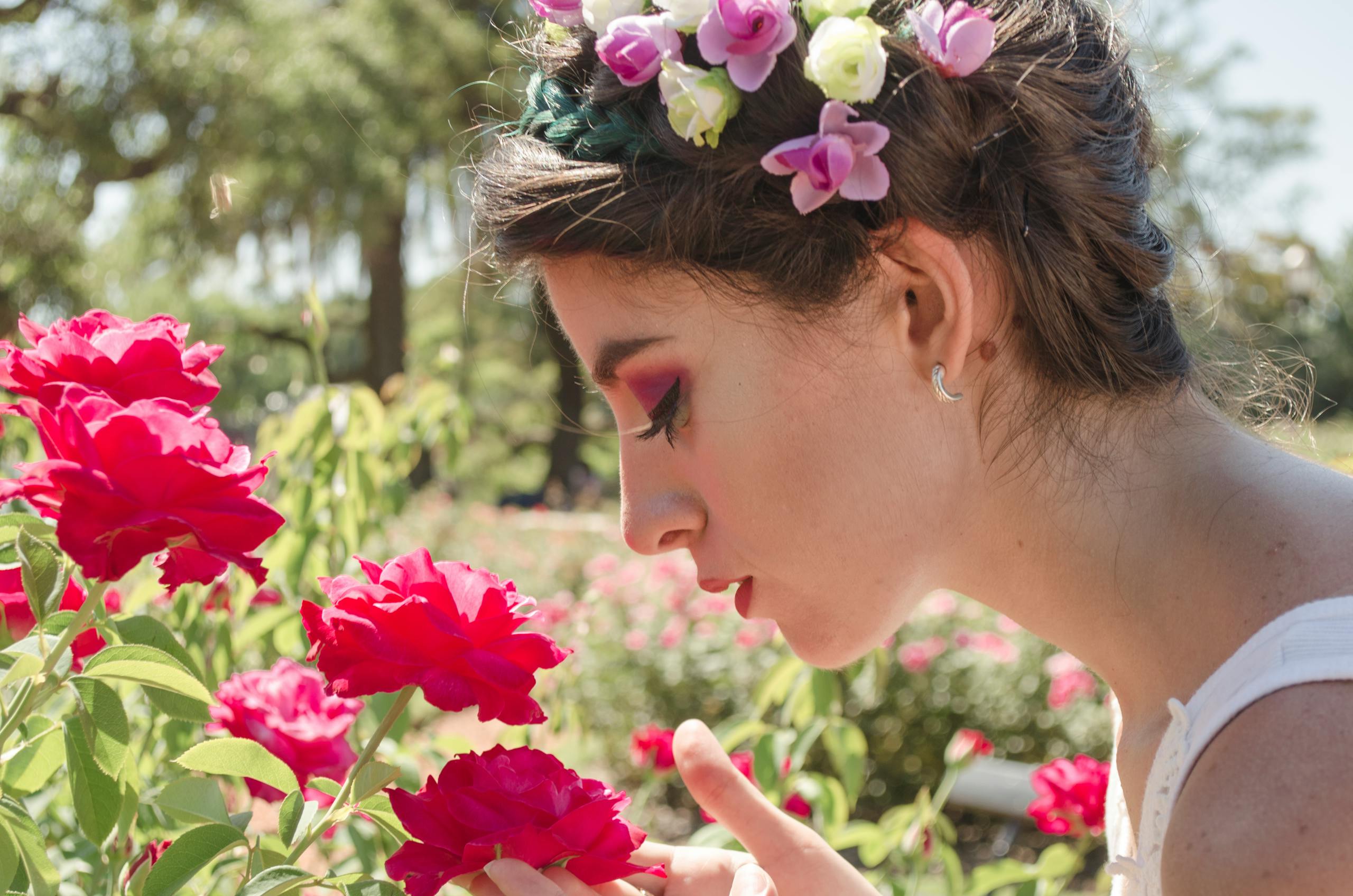 A woman with a floral crown enjoys the fragrant roses in a sunny garden setting.