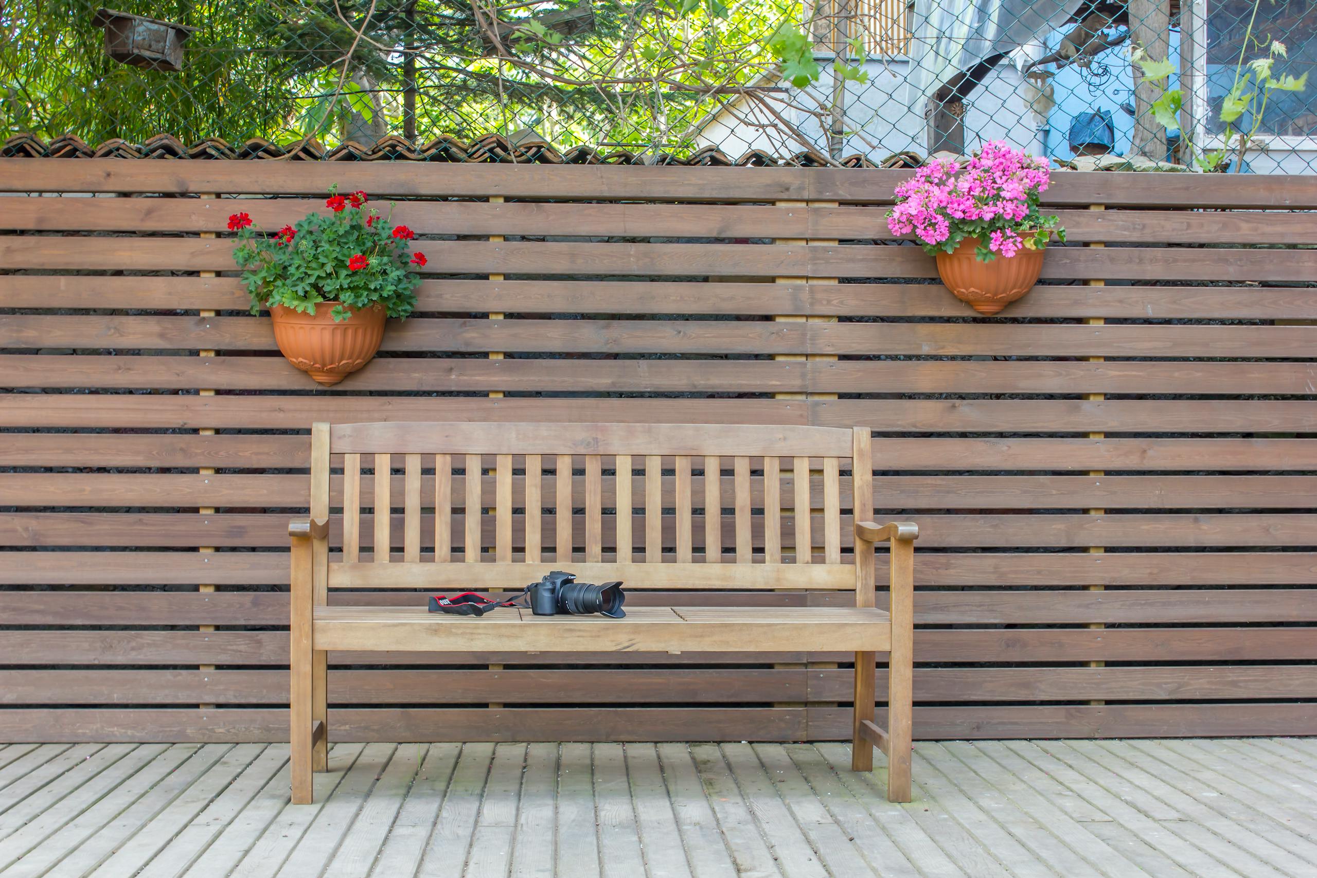 A wooden bench with potted flowers against a wooden fence in a peaceful backyard setting.