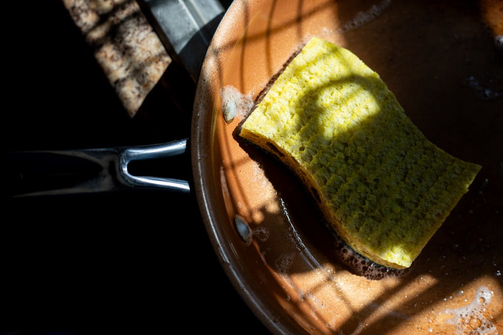 A yellow sponge rests in a copper pan, lit by dramatic shadows. Ideal for cleaning themes.