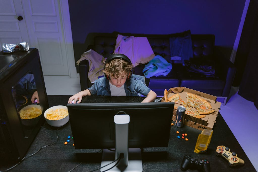 A young boy plays video games at home, surrounded by snacks, showcasing the gaming lifestyle.