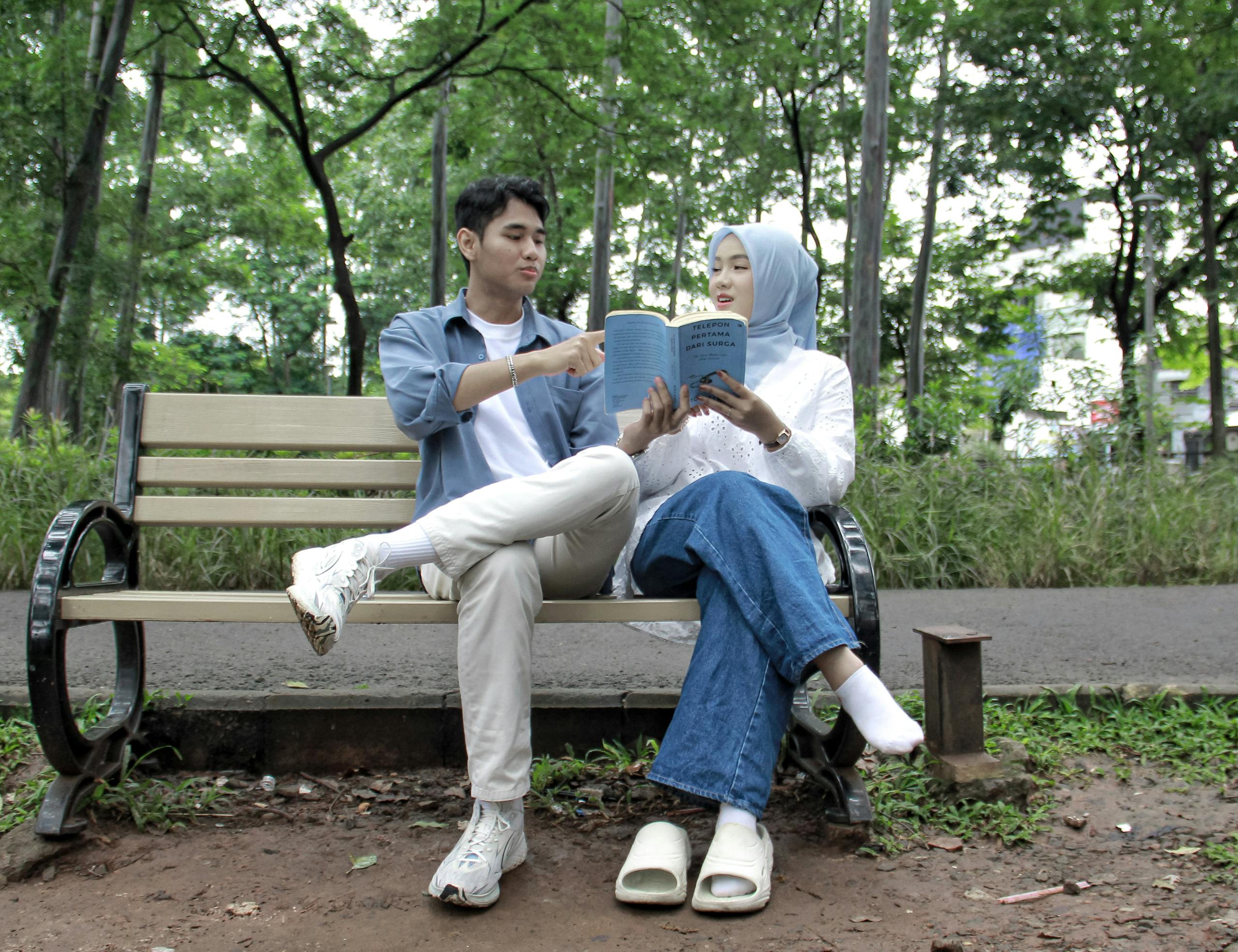 A young couple enjoys reading a book together on a bench in a lush Jakarta park, Indonesia.