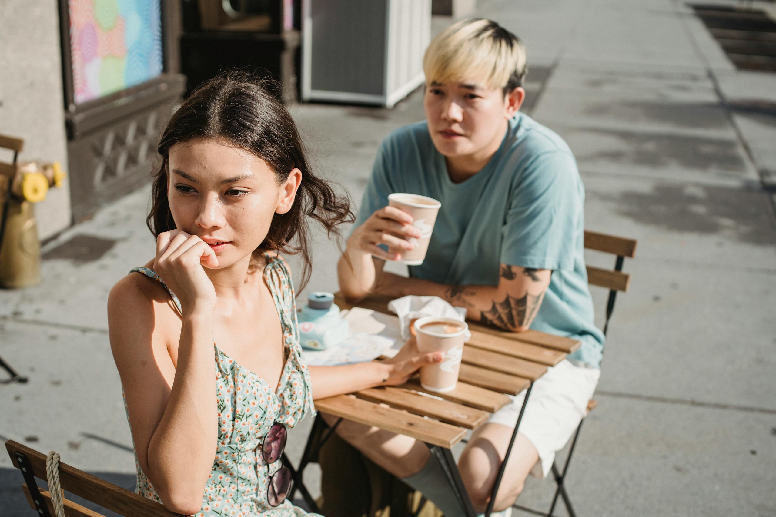 A young couple sitting at a wooden table enjoying coffee outdoors on a sunny day.