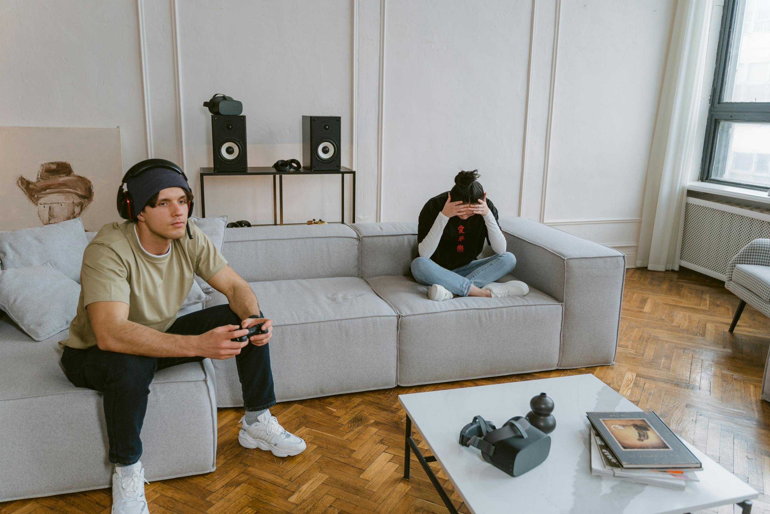 A young man playing video games while a woman relaxes in a modern living room.
