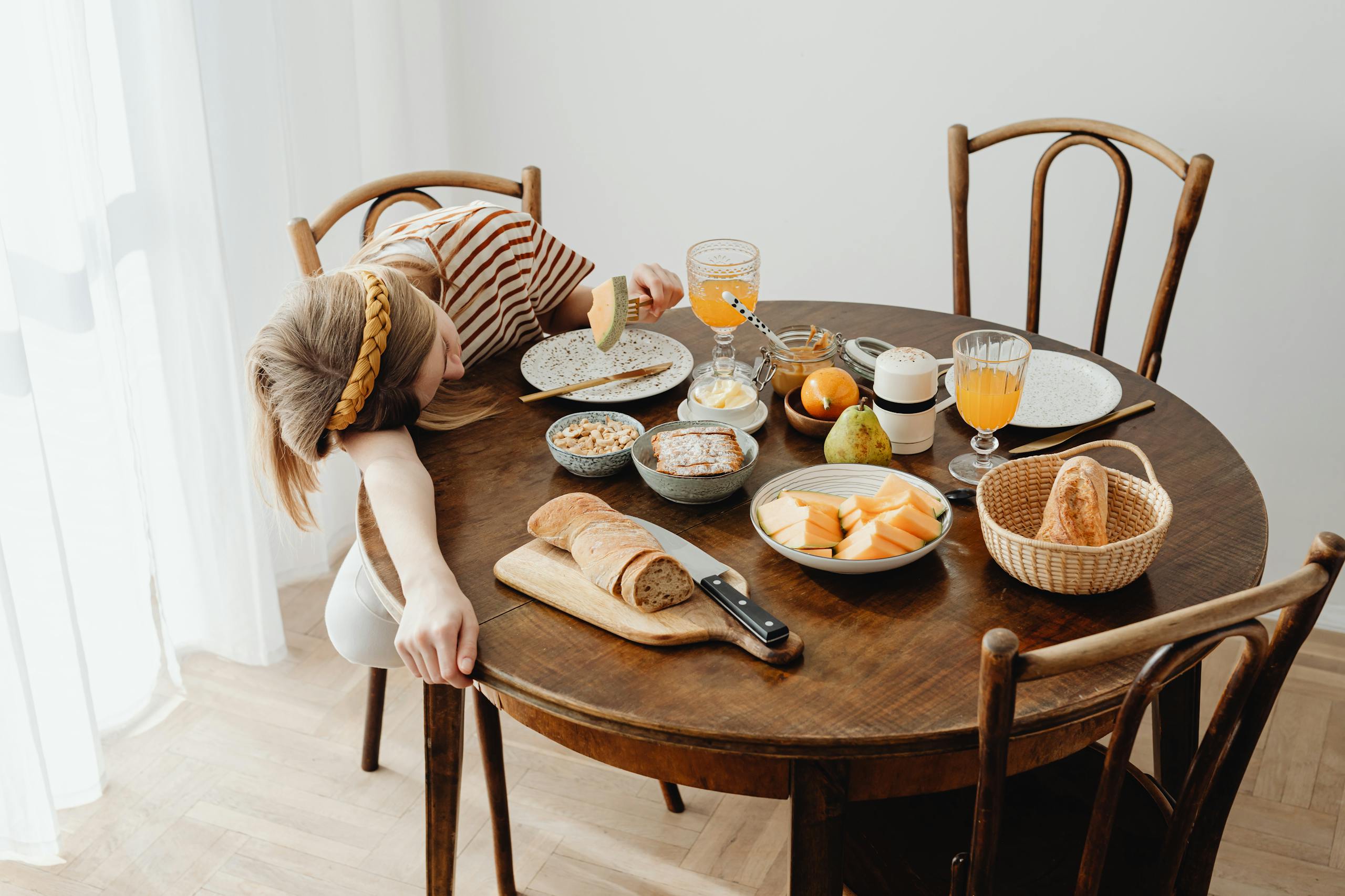 A young woman asleep on a breakfast table surrounded by food, conveying tiredness and leisure.