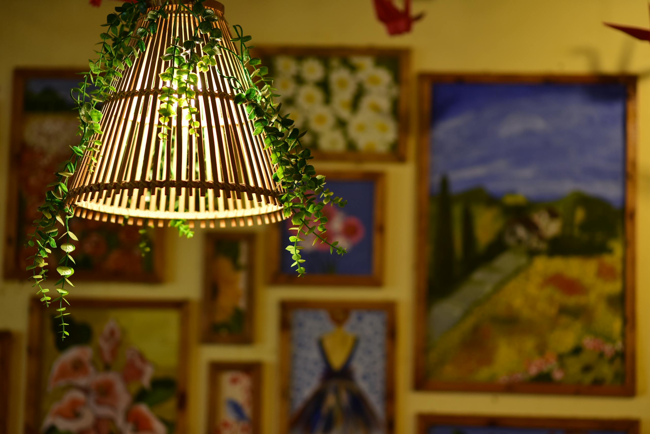 Bamboo lamp with greenery illuminating a gallery wall adorned with vibrant paintings, creating a cozy ambiance.