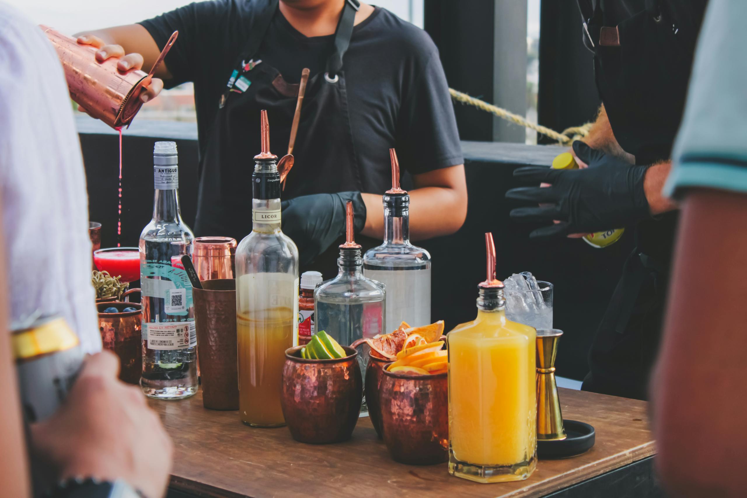 Bartender skillfully prepares vibrant cocktails at a rooftop bar with an array of spirits.
