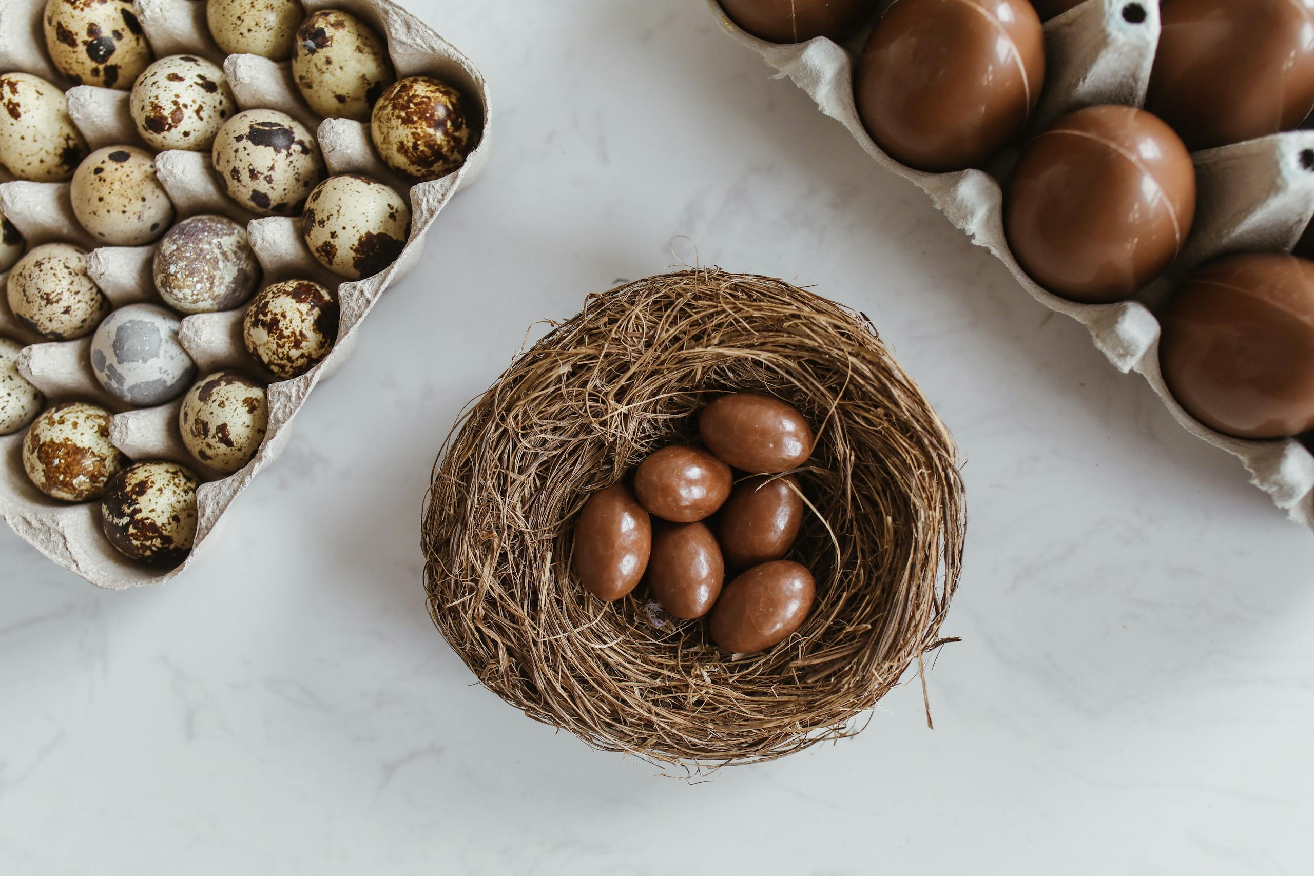 Bird's nest with chocolate eggs beside real eggs on a marble surface creates a rustic feel.