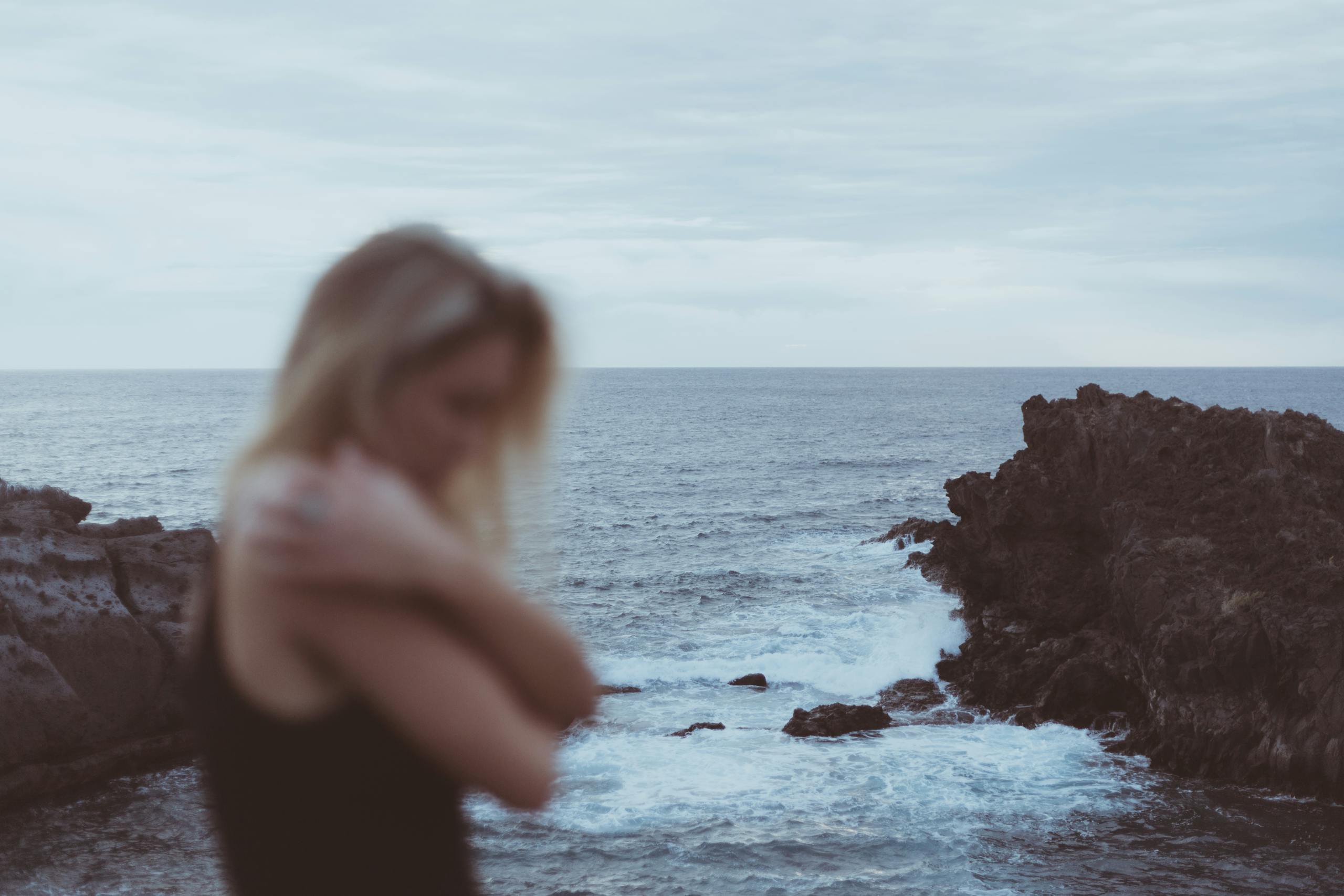 Blurred woman by rocky seashore in Canary Islands, capturing a peaceful and dramatic ocean scene.
