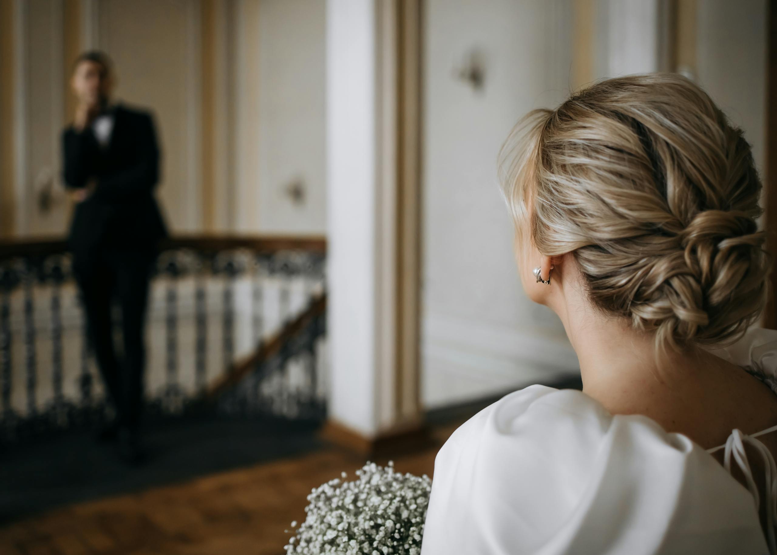 Bride with elegantly styled hair holding floral bouquet, gazing at groom.