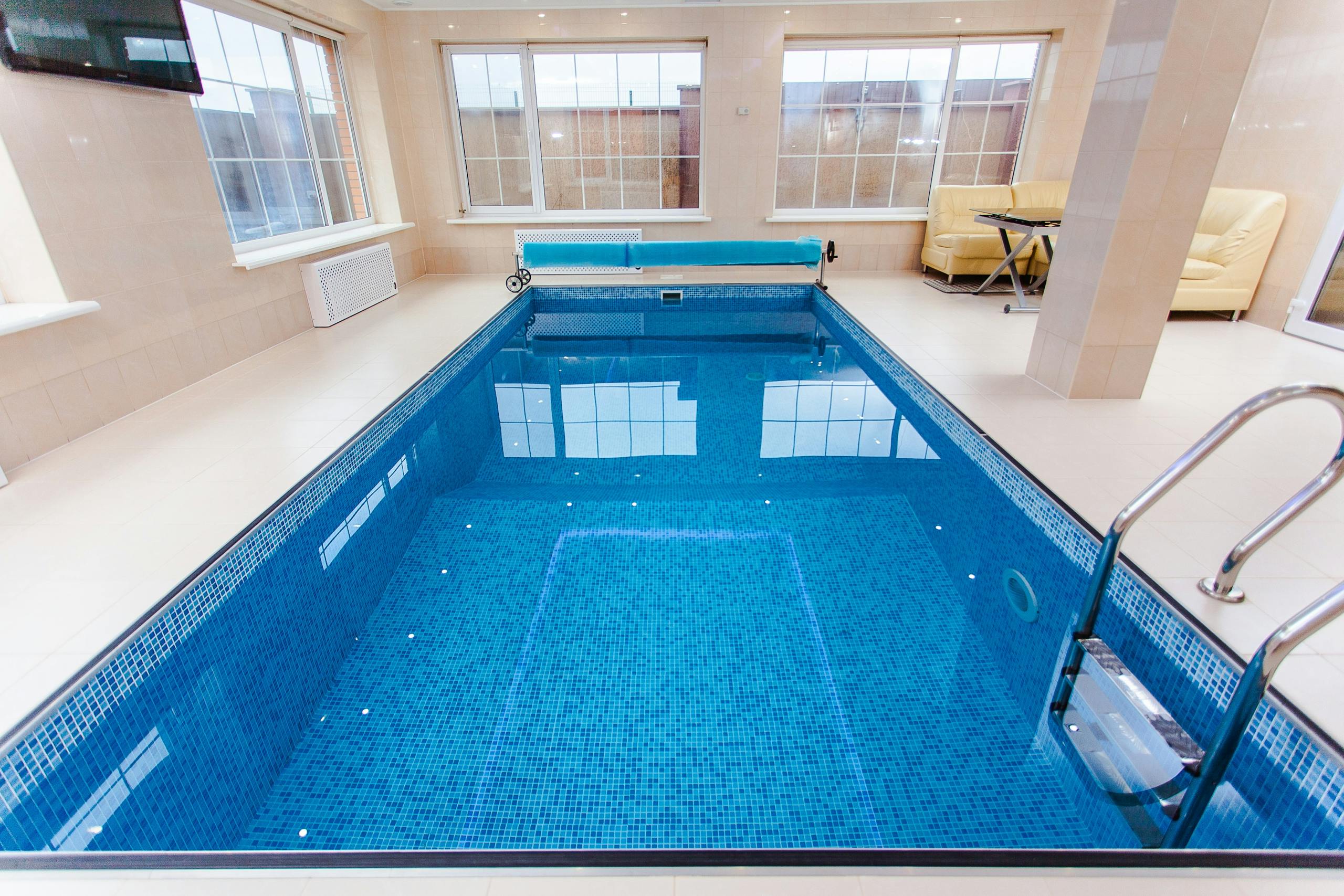 Bright indoor swimming pool with luxury seating and large windows.