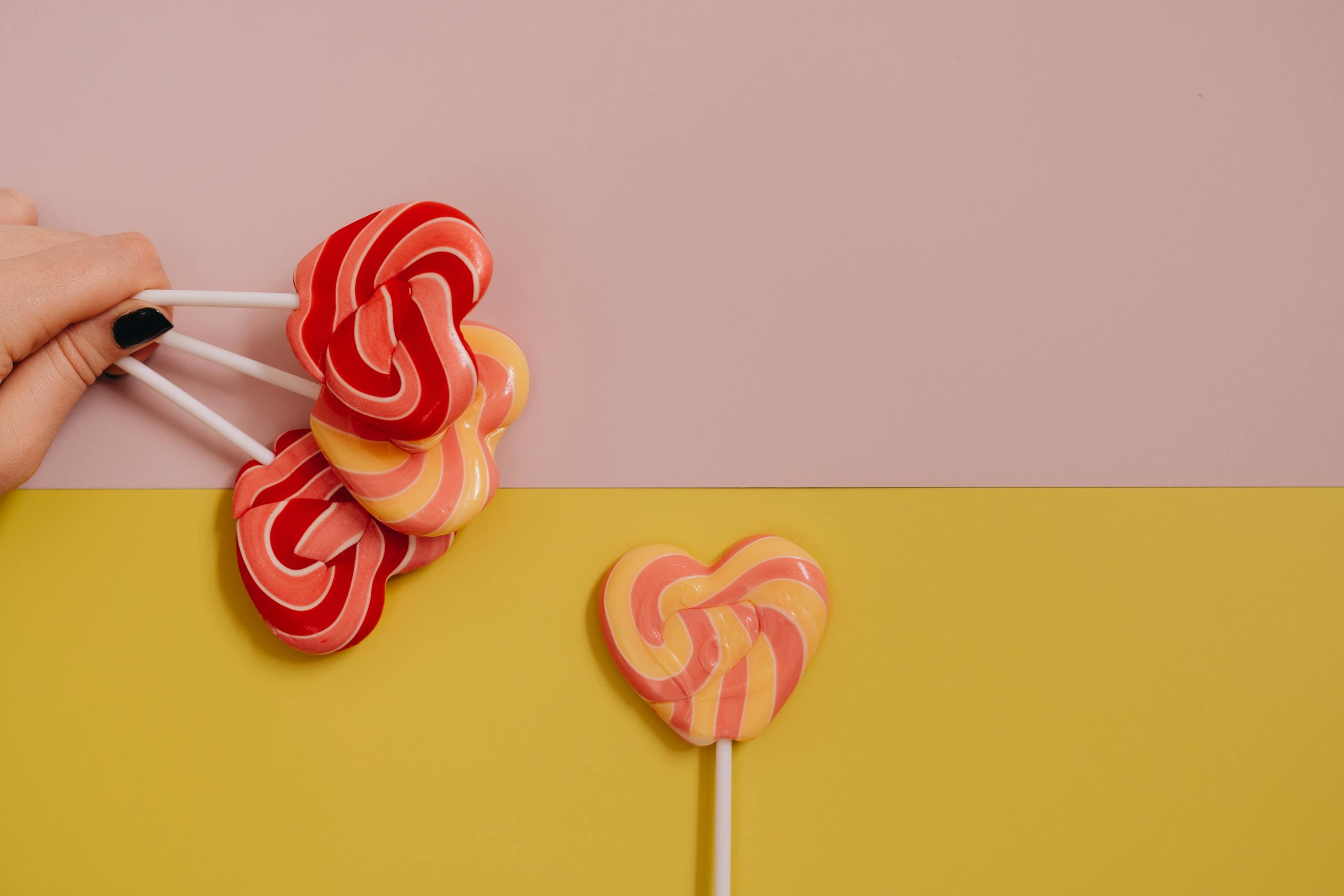 Brightly colored heart-shaped lollipops on a vibrant pastel background with copy space.