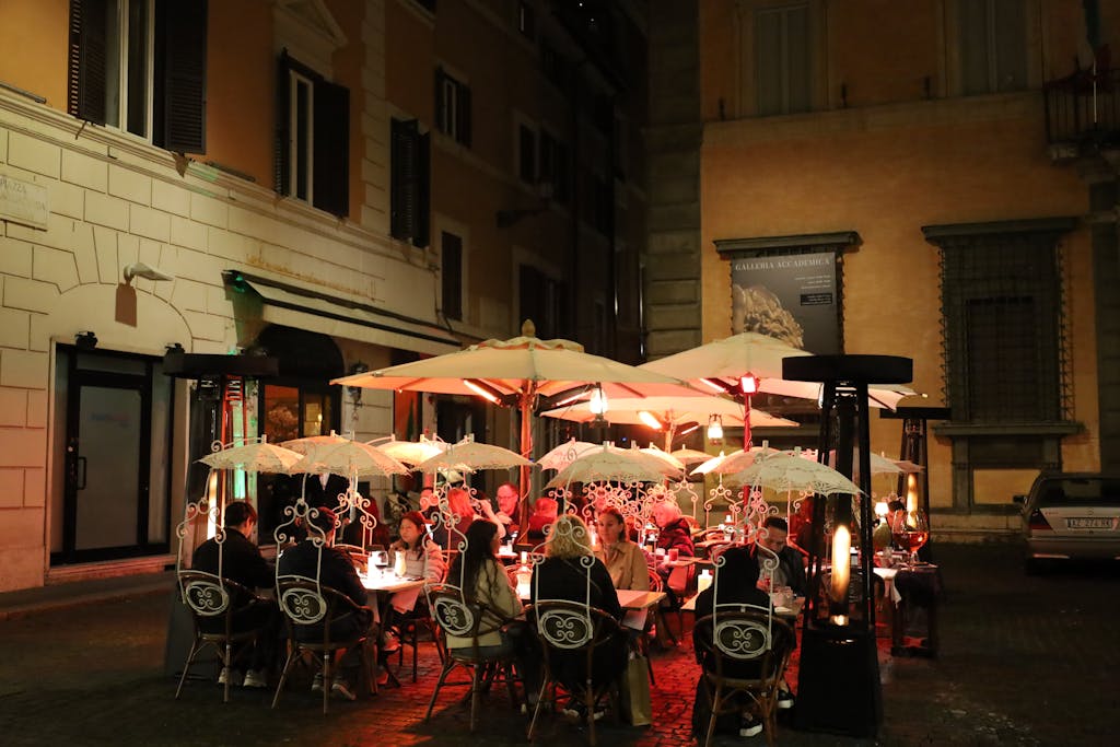 Capture of a lively outdoor dining scene in Rome, featuring umbrellas and warm lighting.