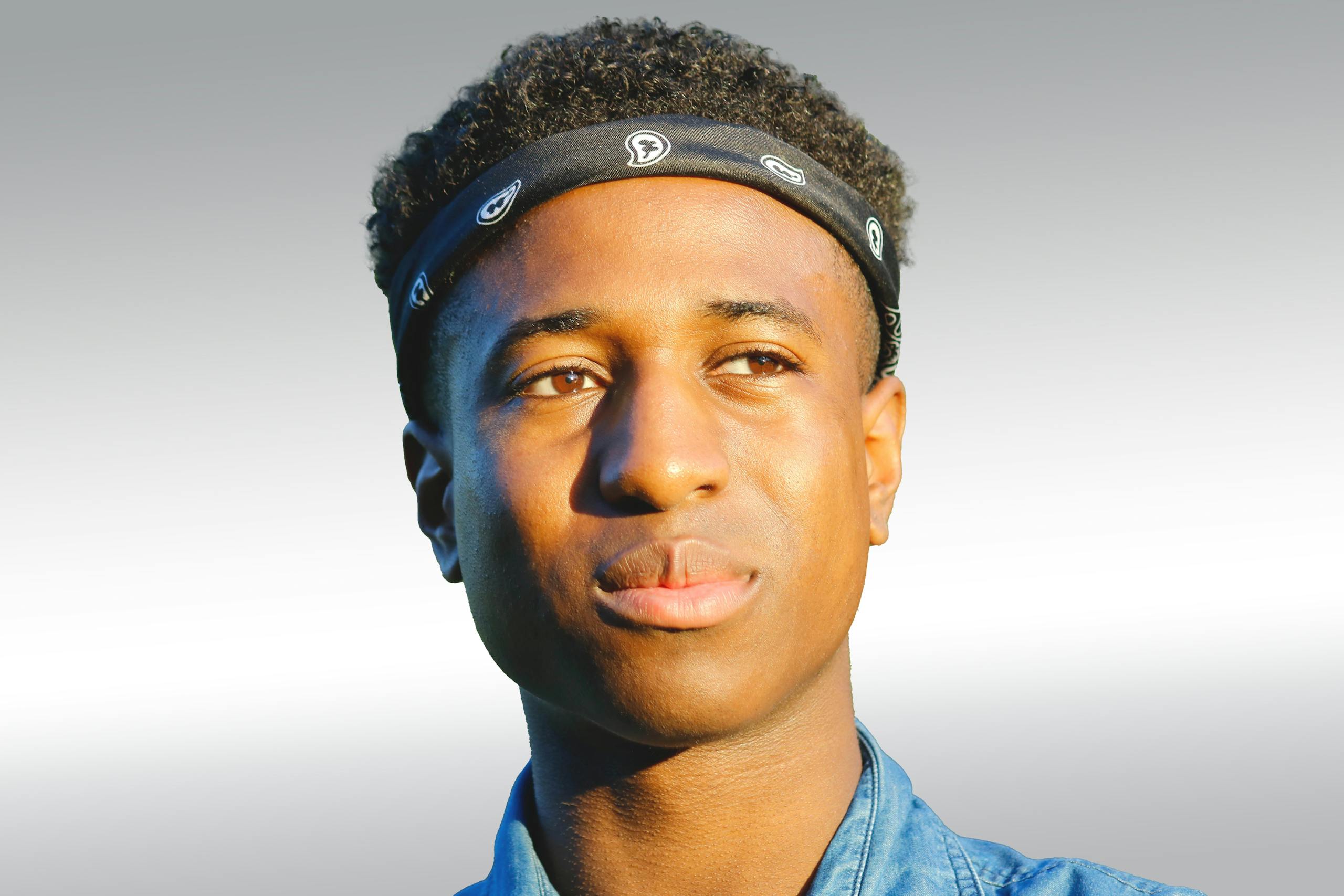 Close-up headshot of a young man with a bandana, bathed in warm sunlight.