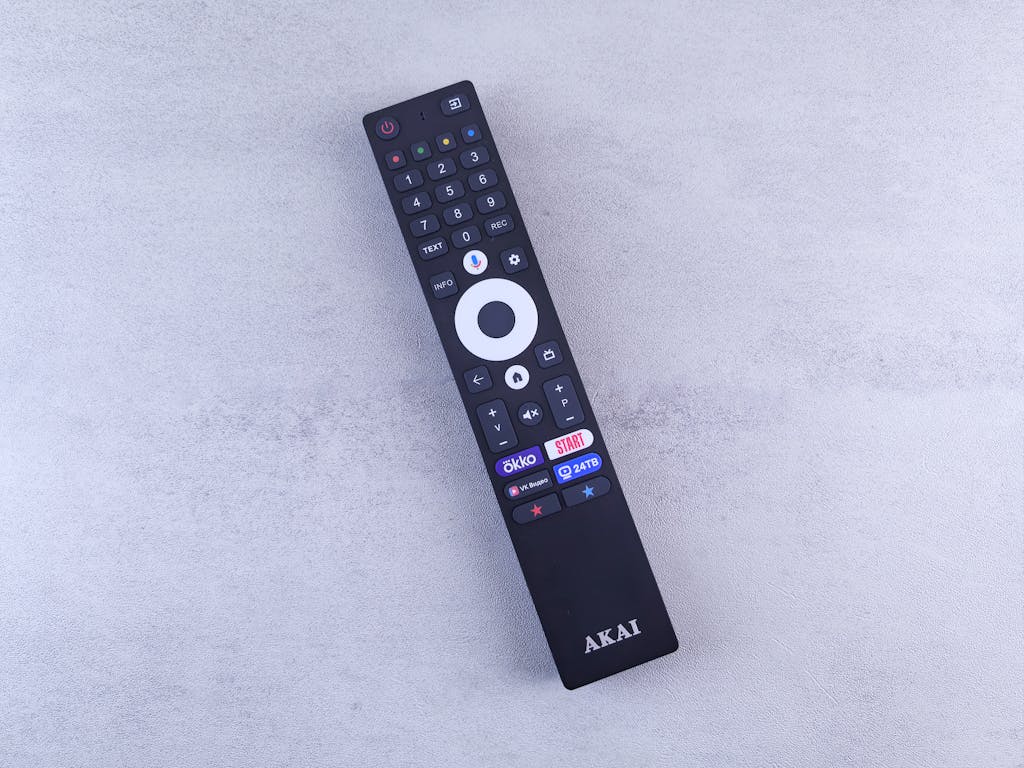 Close-up of a black remote control against a light textured backdrop, highlighting buttons and brand.