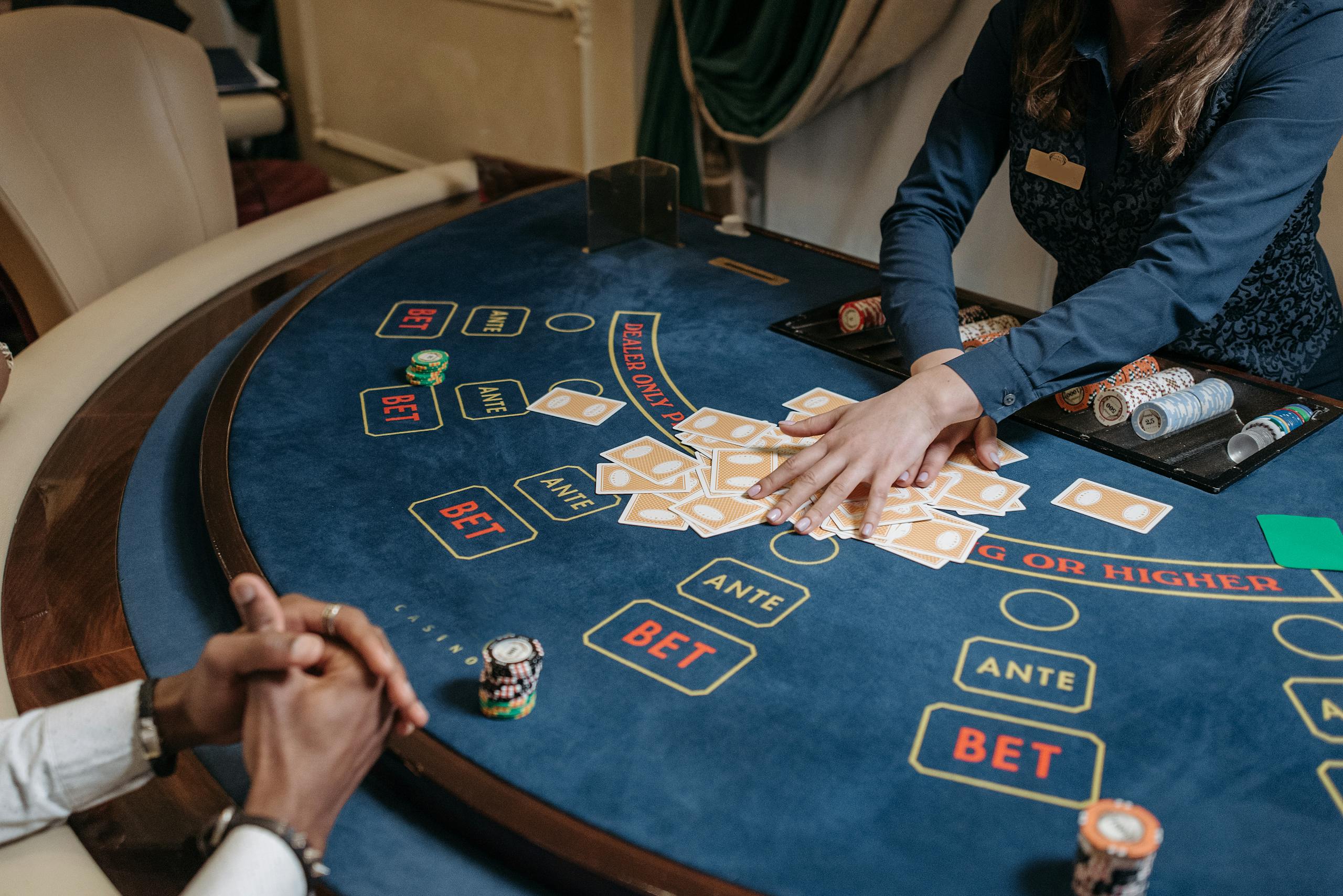 Close-up of a casino dealer shuffling cards on a gambling table with chips and bet labels.