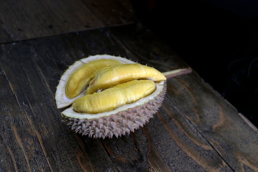 Close-up of a durian fruit split open, revealing yellow flesh on a wooden surface.