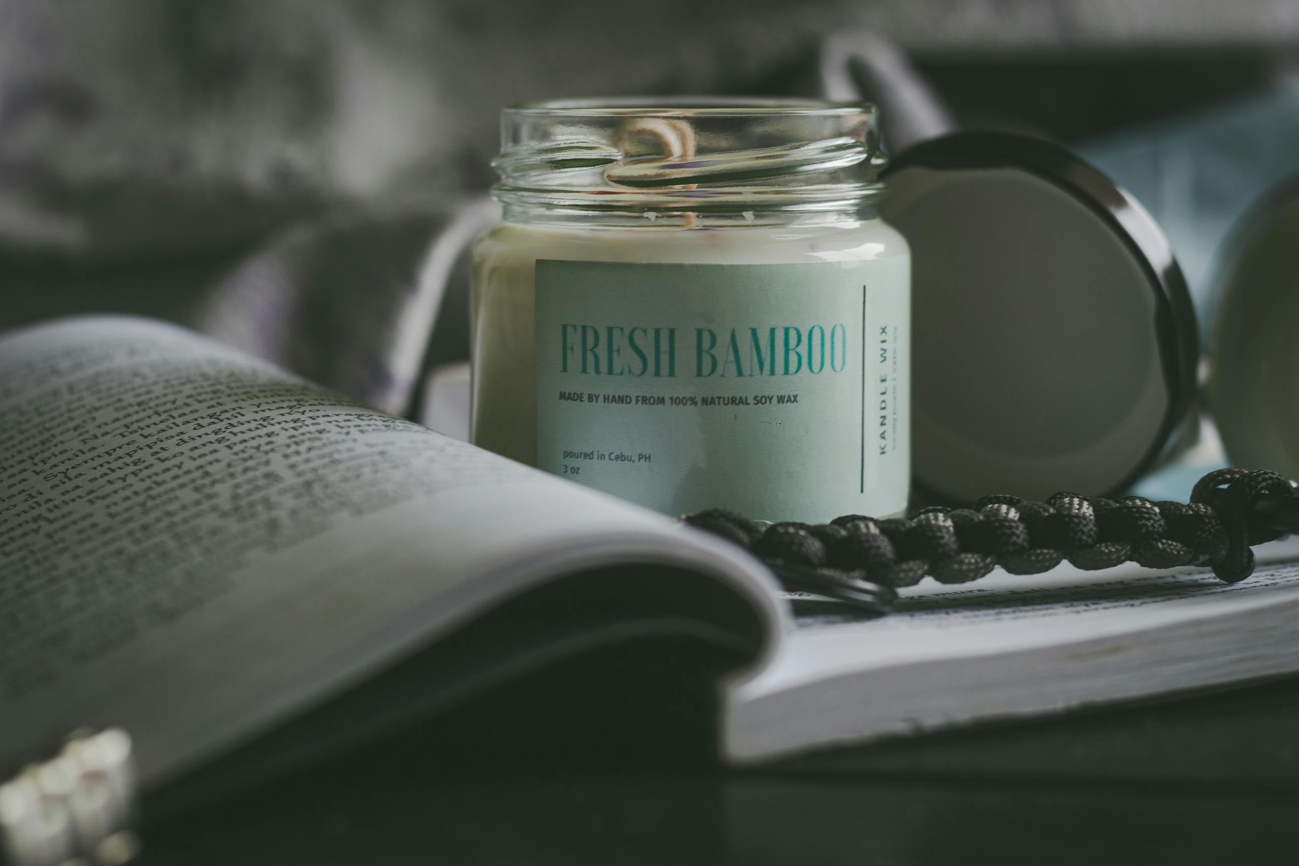 Close-up of a fresh bamboo scented candle surrounded by books, creating a cozy atmosphere.