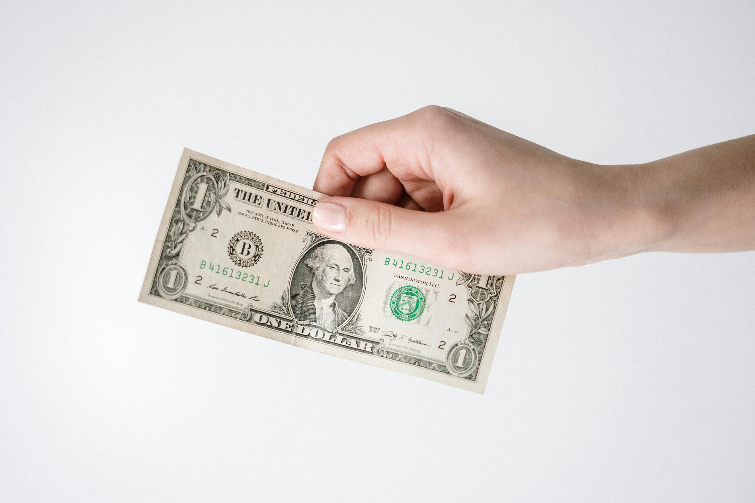 Close-up of a hand holding a one US dollar bill against a white background. Ideal for finance-related themes.
