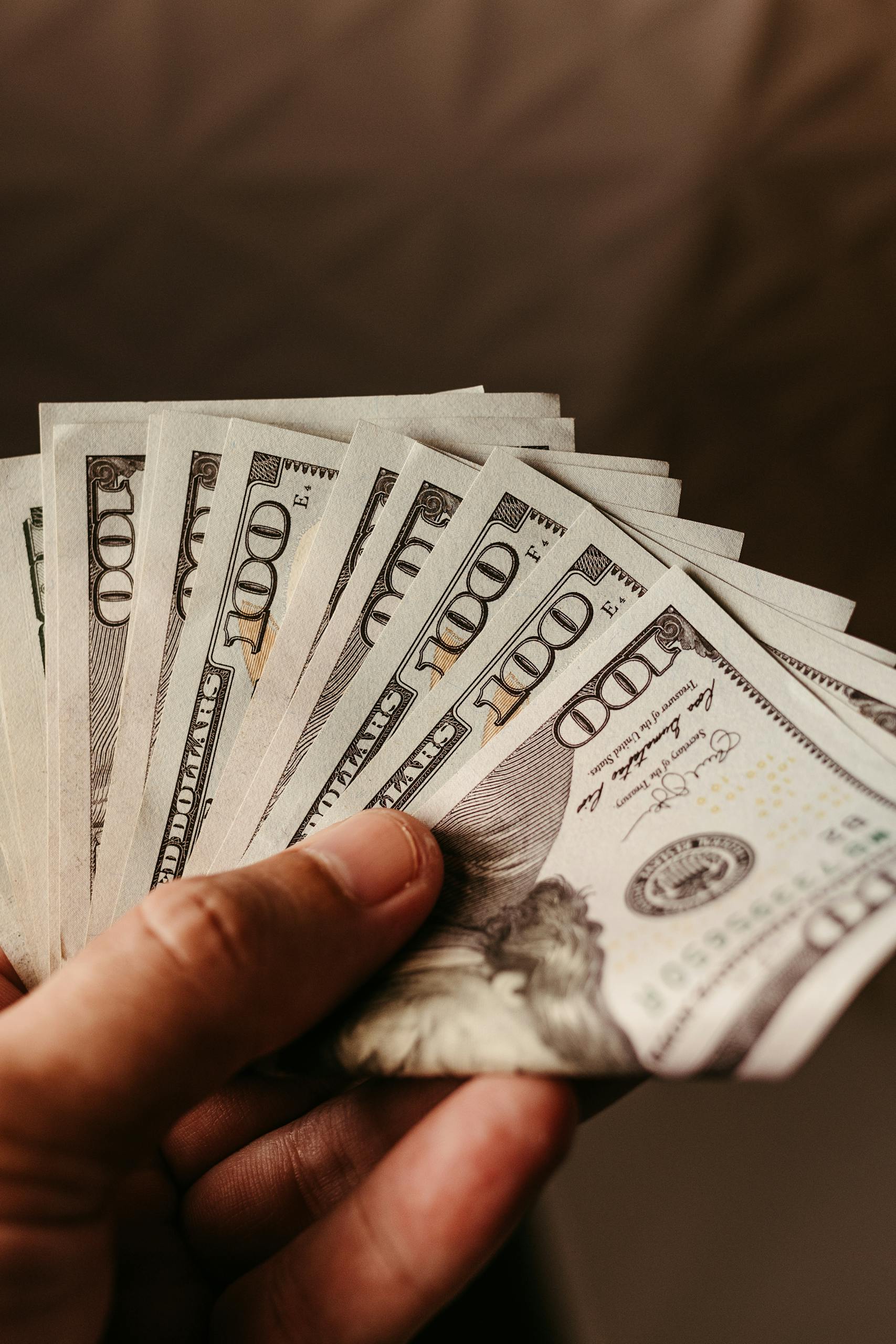 Close-up of a hand holding several hundred dollar bills, representing wealth and finance.