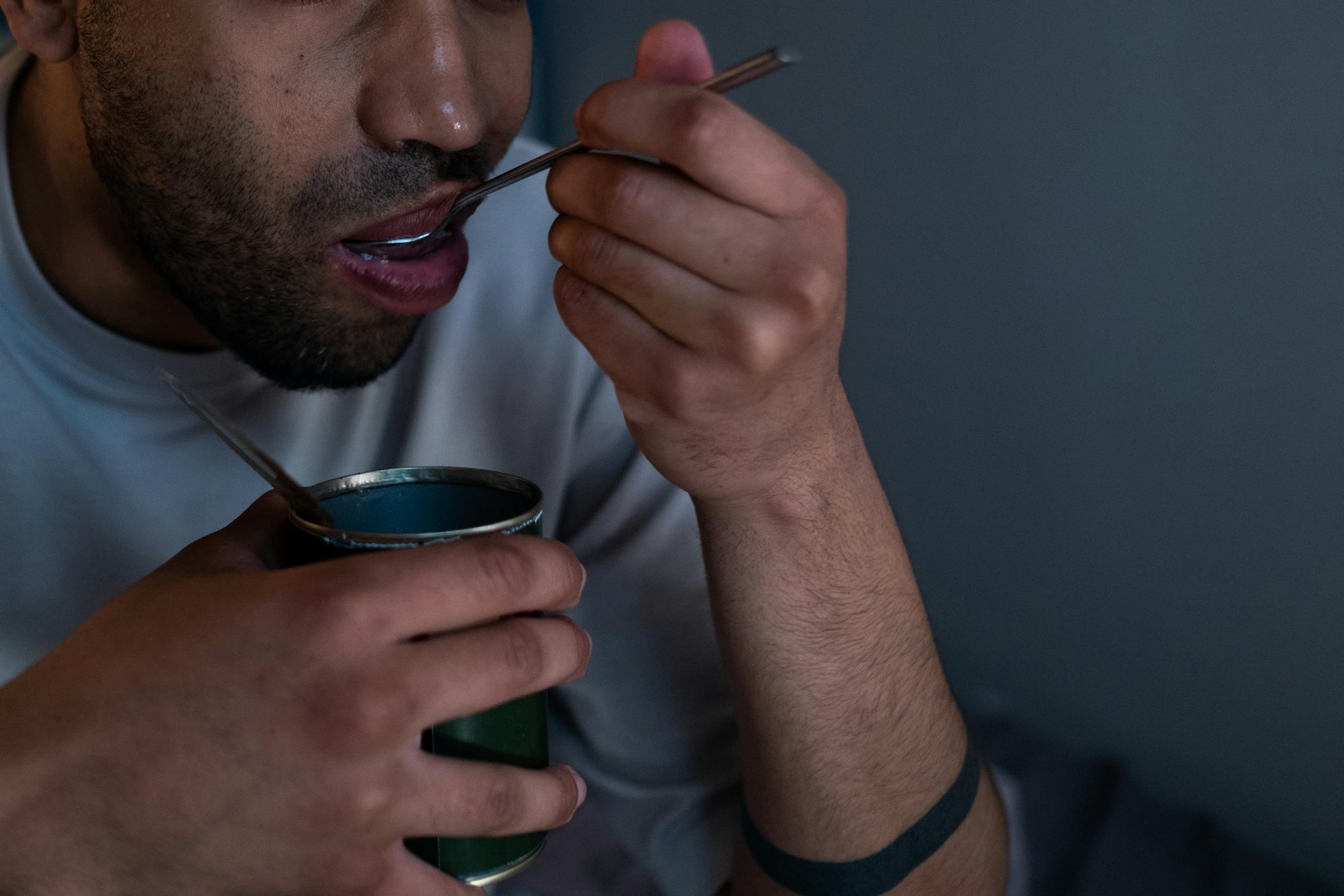 Close-up of a man eating canned food at home, highlighting quarantine lifestyle during isolation.