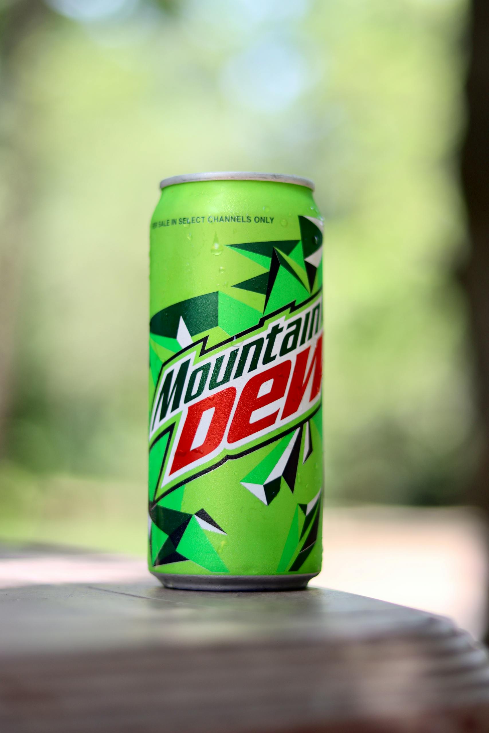Close-up of a Mountain Dew can on a table with a blurred outdoor background.