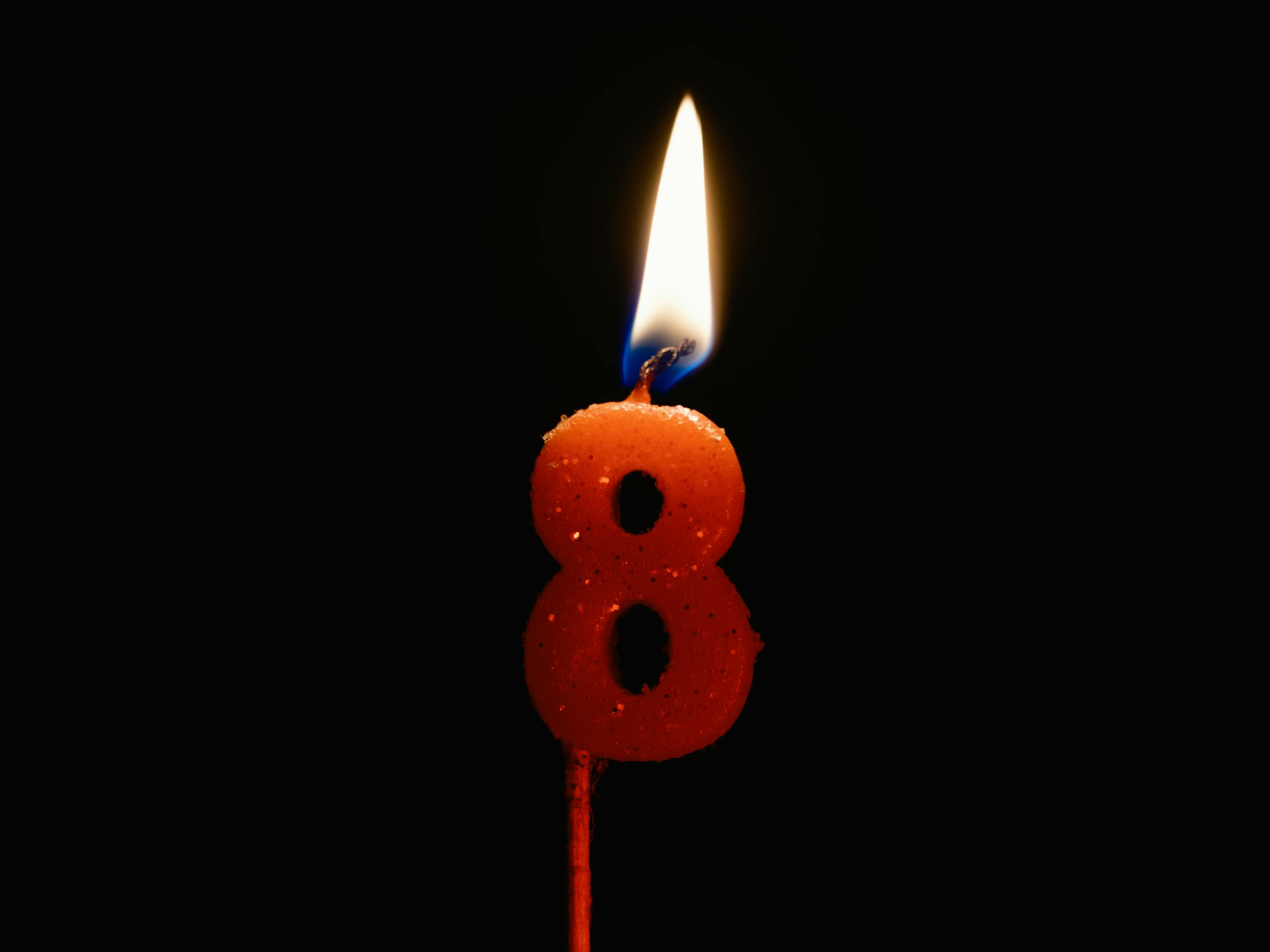 Close-up of a number 8 candle lit against a black background, creating a warm glow.