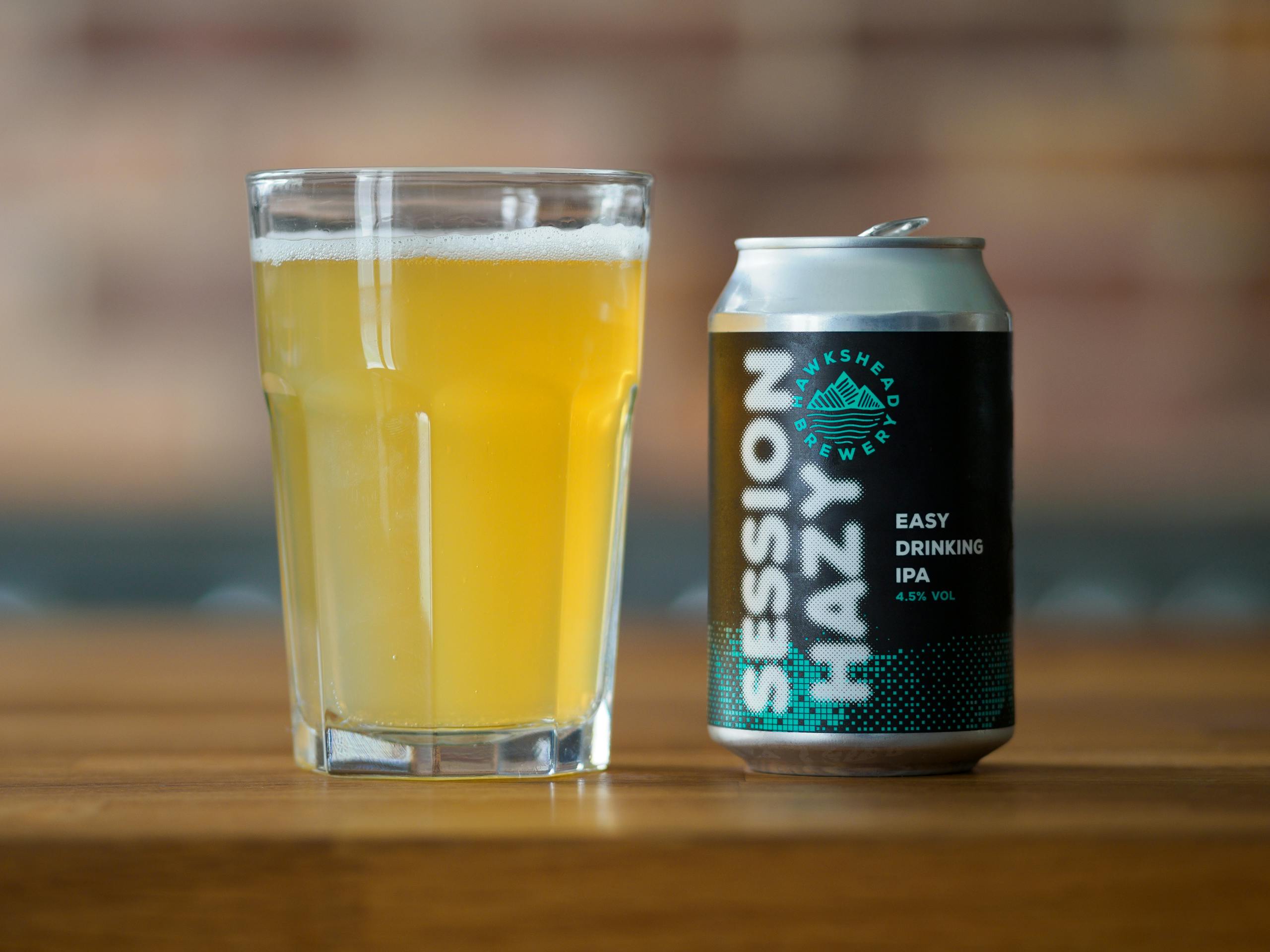 Close-up of a Session Hazy IPA can and glass with beer on a wooden table.